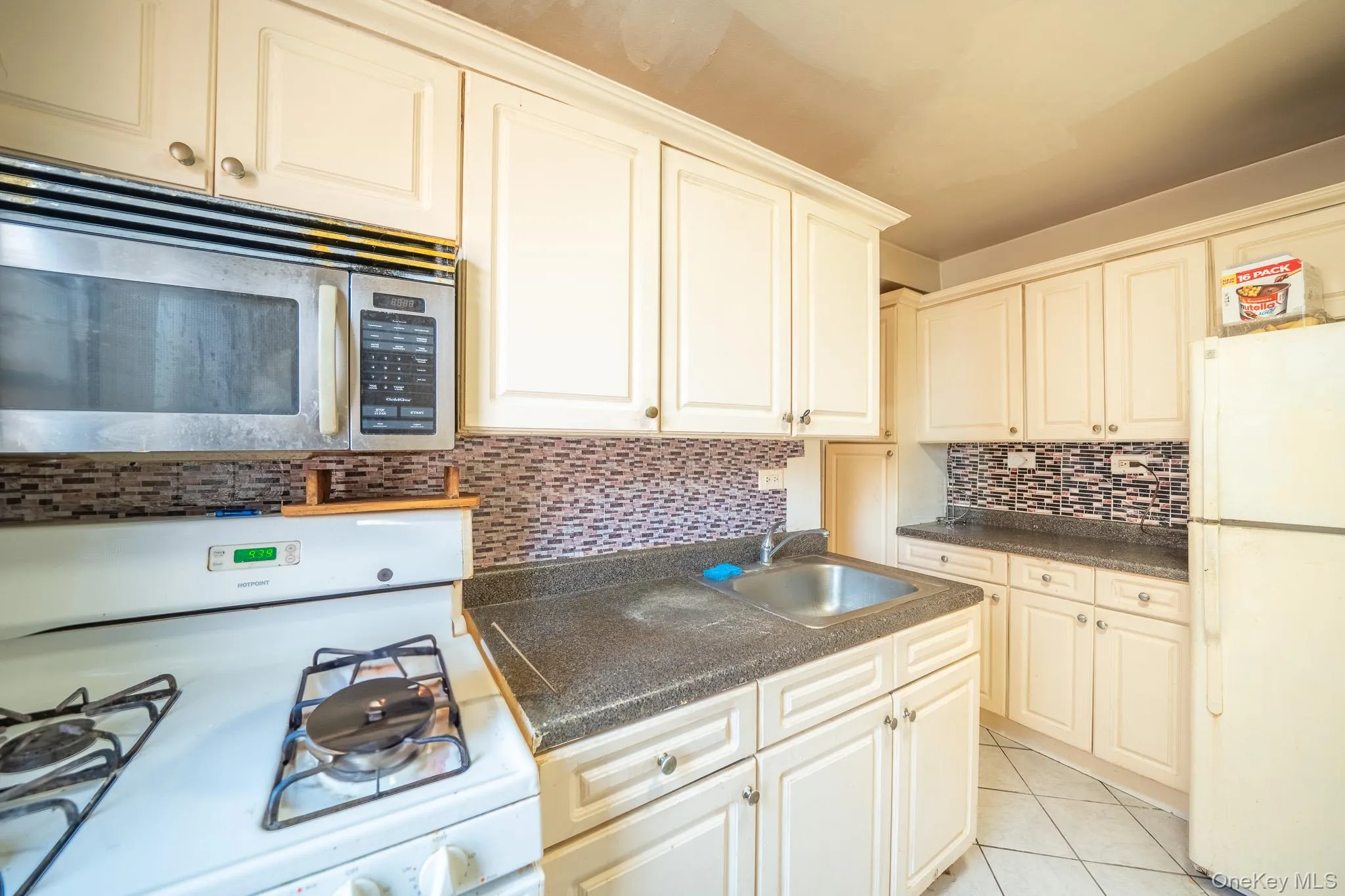 Kitchen with white appliances, backsplash, dark countertops, and light tile patterned flooring Kitchen with white appliances, backsplash, dark countertops, and light tile patterned flooring
