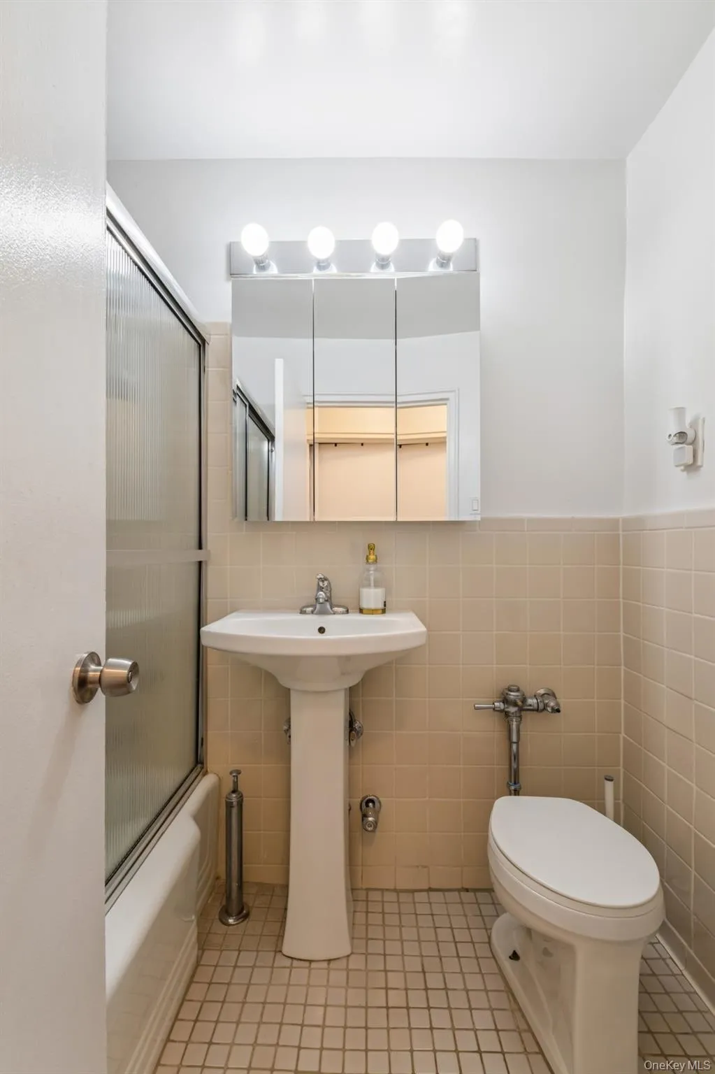 Full bath with tile walls, bath / shower combo with glass door, tile patterned floors, and wainscoting Full bath with tile walls, bath / shower combo with glass door, tile patterned floors, and wainscoting