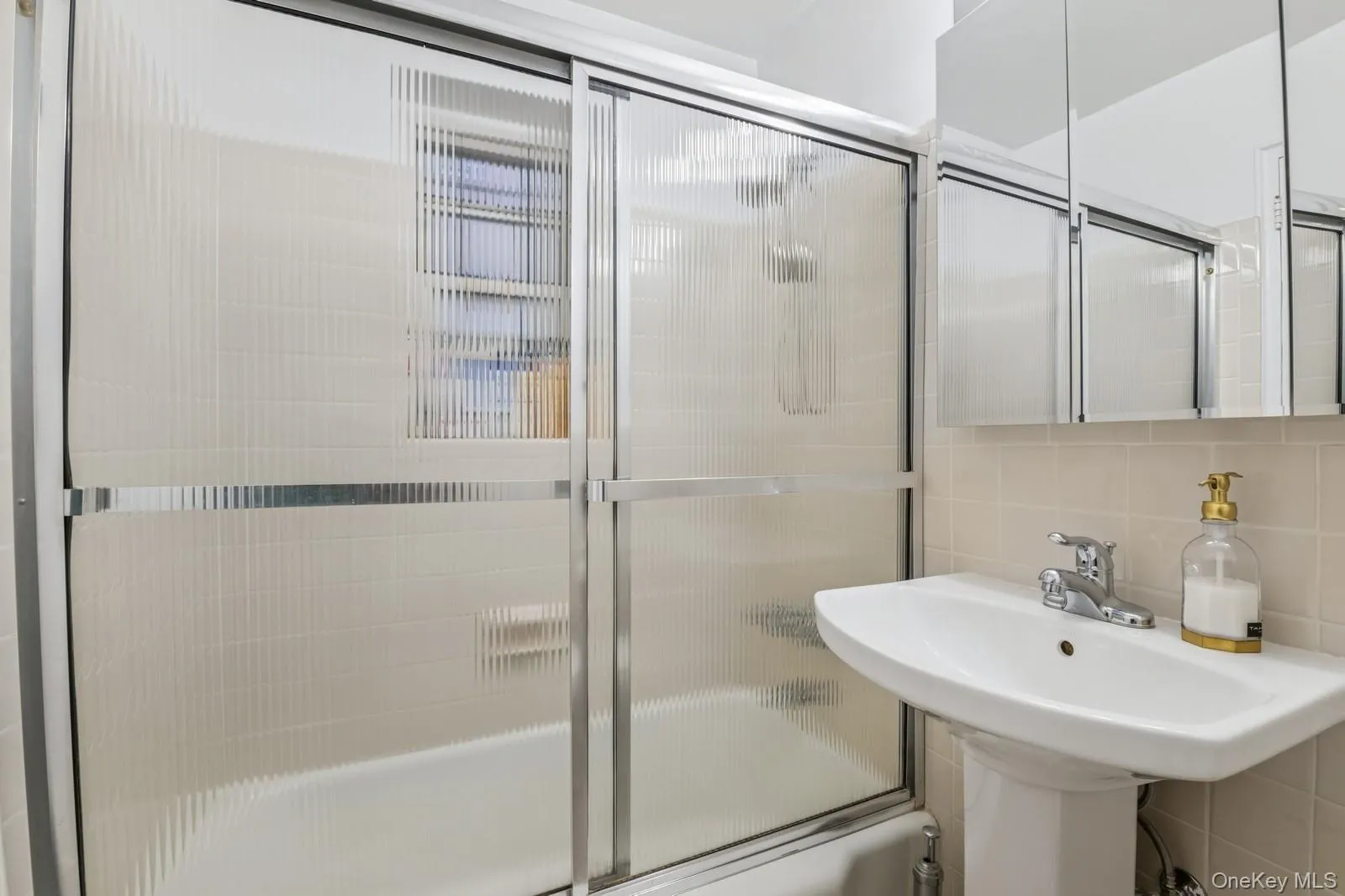 Bathroom featuring enclosed tub / shower combo, decorative backsplash, and tile walls Bathroom featuring enclosed tub / shower combo, decorative backsplash, and tile walls