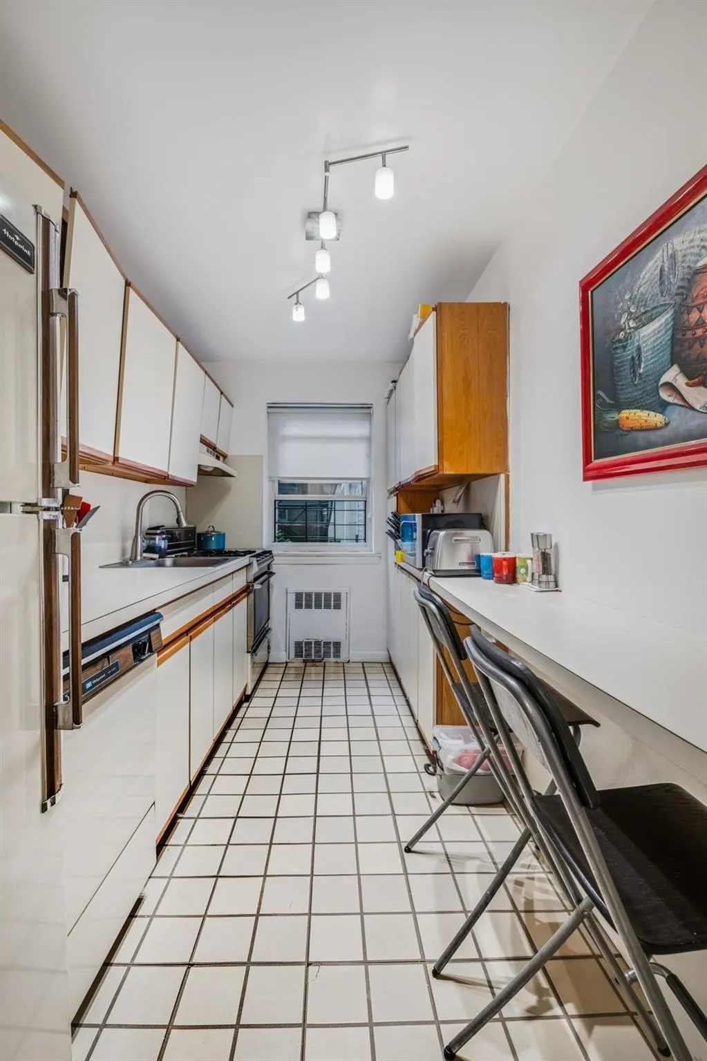 Kitchen featuring light countertops, white cabinetry, light tile patterned floors, radiator, and white appliances Kitchen featuring light countertops, white cabinetry, light tile patterned floors, radiator, and white appliances