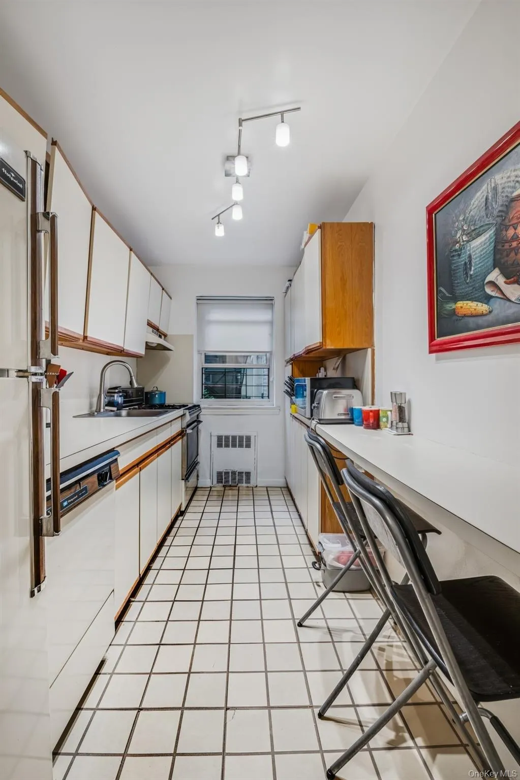 Kitchen featuring light countertops, white cabinetry, light tile patterned floors, radiator, and white appliances Kitchen featuring light countertops, white cabinetry, light tile patterned floors, radiator, and white appliances