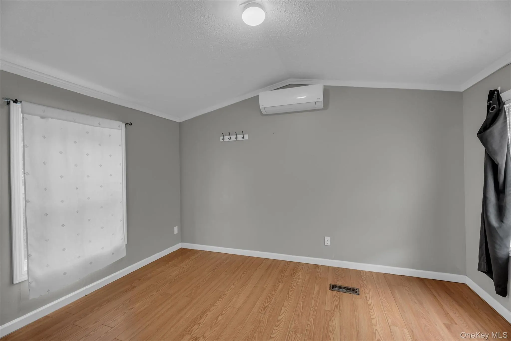 Spare room with ornamental molding, wood finished floors, an AC wall unit, and lofted ceiling Spare room with ornamental molding, wood finished floors, an AC wall unit, and lofted ceiling