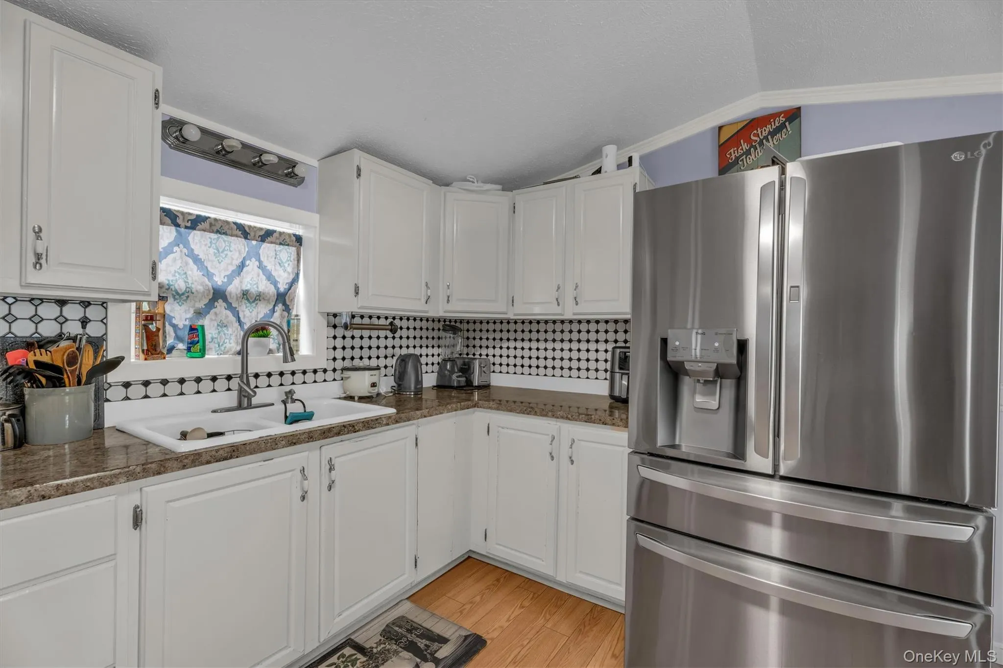 Kitchen with stainless steel fridge, decorative backsplash, vaulted ceiling, white cabinets, and light wood-style floors Kitchen with stainless steel fridge, decorative backsplash, vaulted ceiling, white cabinets, and light wood-style floors
