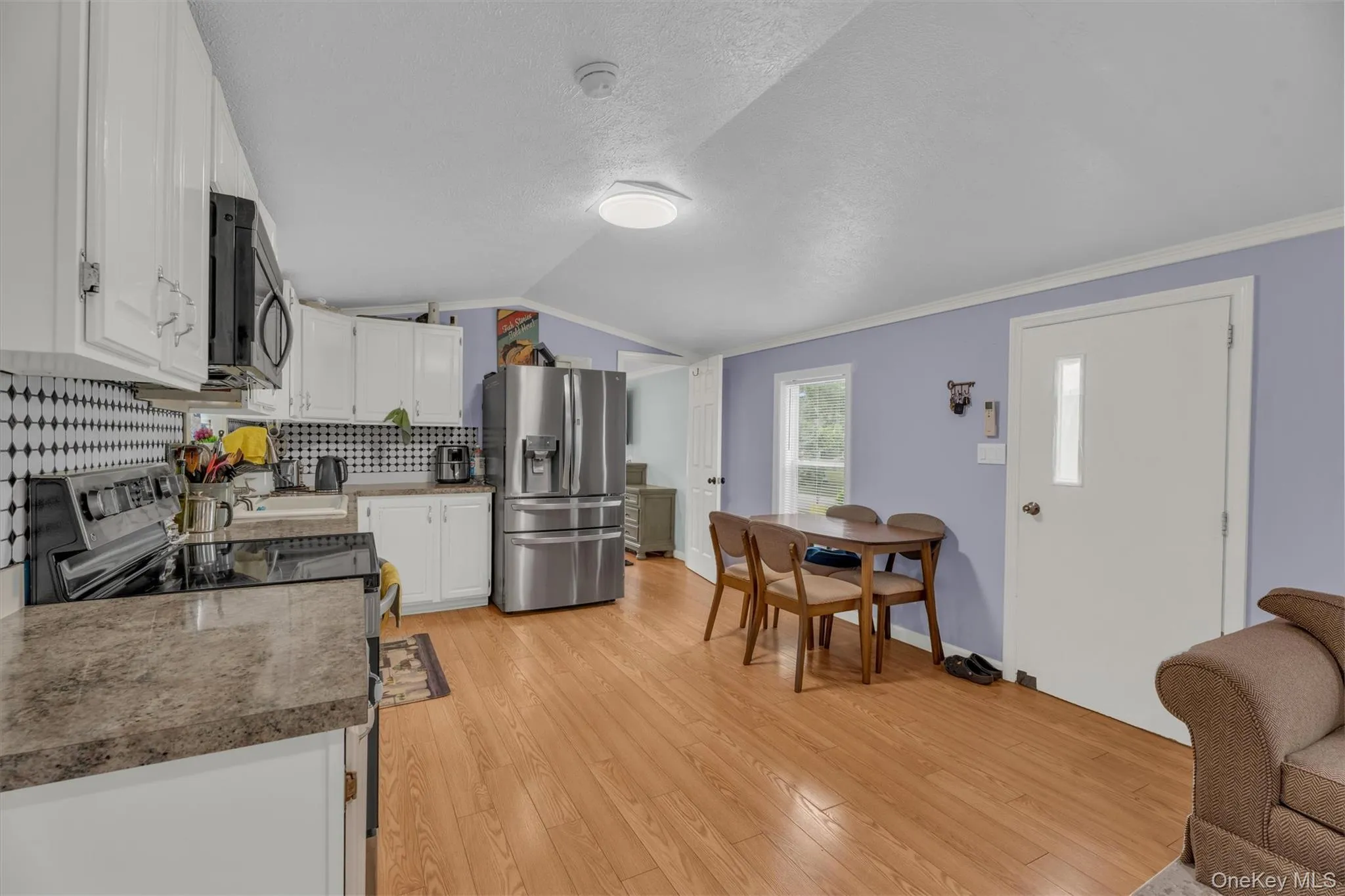 Kitchen featuring stainless steel appliances, white cabinets, light wood-style flooring, backsplash, and lofted ceiling Kitchen featuring stainless steel appliances, white cabinets, light wood-style flooring, backsplash, and lofted ceiling
