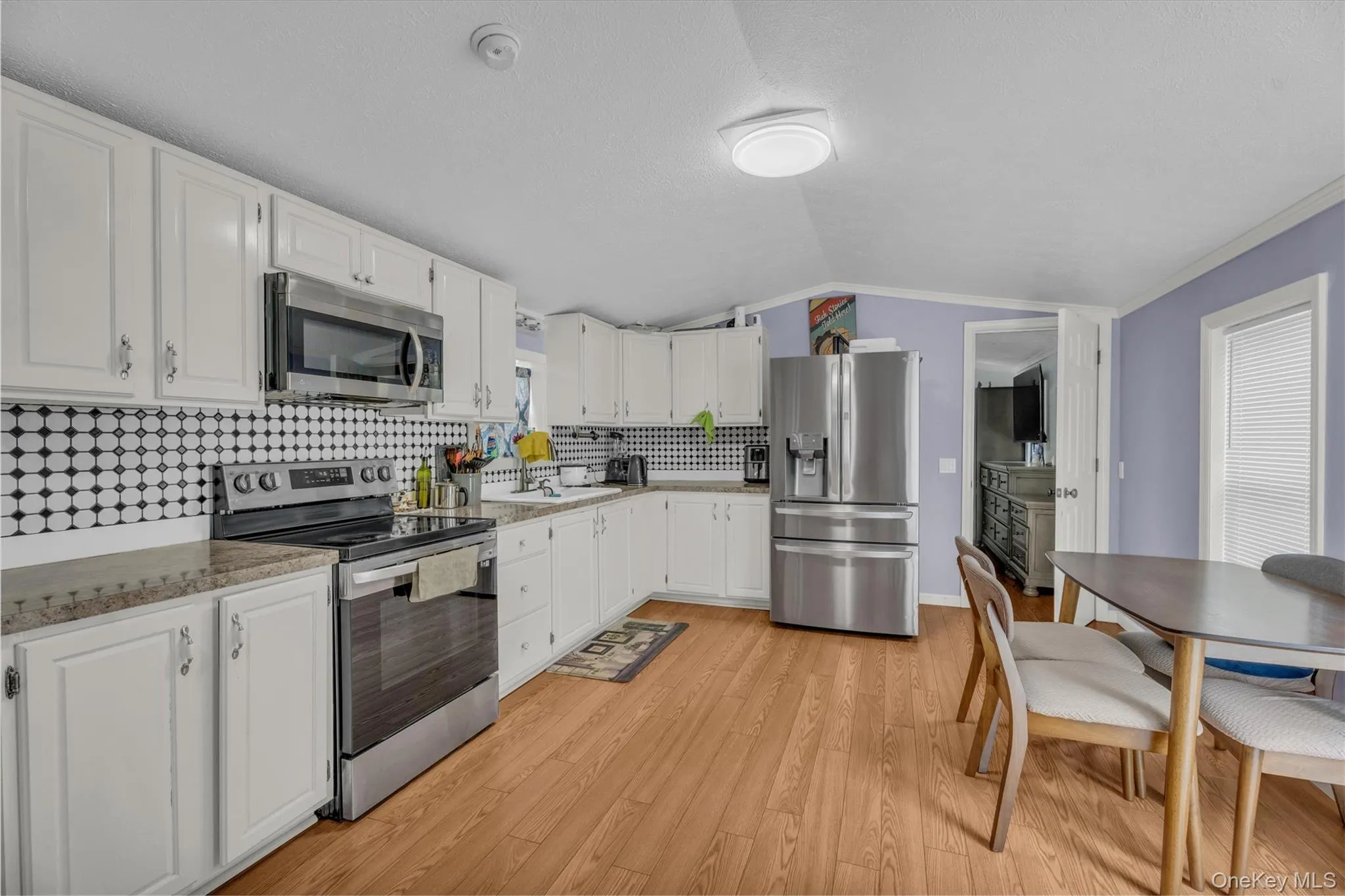 Kitchen with stainless steel appliances, tasteful backsplash, white cabinets, light wood-style floors, and vaulted ceiling Kitchen with stainless steel appliances, tasteful backsplash, white cabinets, light wood-style floors, and vaulted ceiling