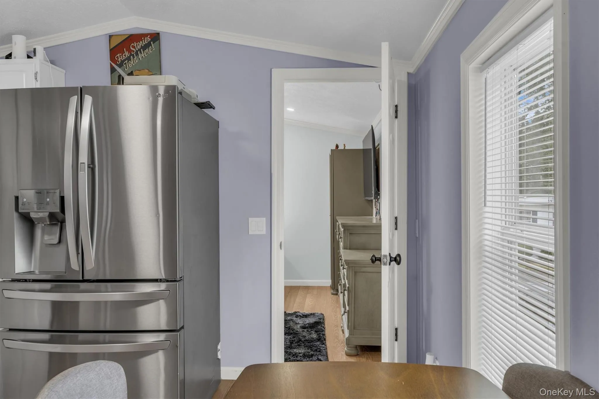 Kitchen featuring stainless steel refrigerator with ice dispenser, crown molding, wood finished floors, and white cabinetry Kitchen featuring stainless steel refrigerator with ice dispenser, crown molding, wood finished floors, and white cabinetry