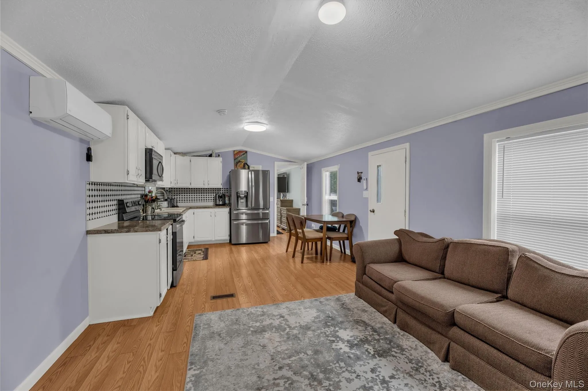 Living area with vaulted ceiling, crown molding, light wood-type flooring, and an AC wall unit Living area with vaulted ceiling, crown molding, light wood-type flooring, and an AC wall unit