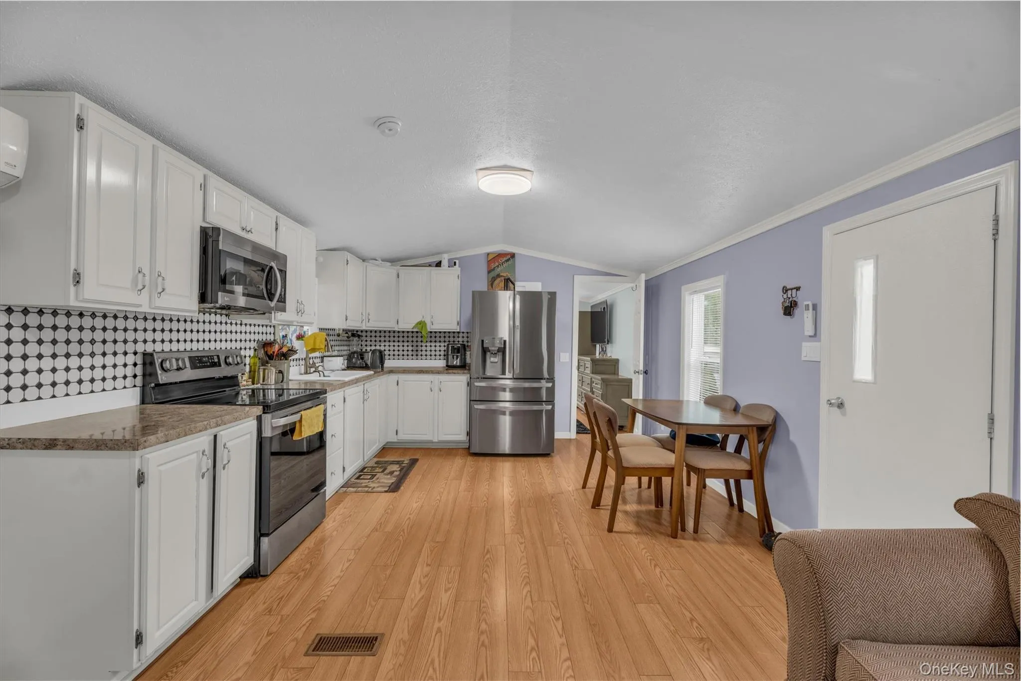 Kitchen featuring appliances with stainless steel finishes, vaulted ceiling, decorative backsplash, light wood-style floors, and white cabinets Kitchen featuring appliances with stainless steel finishes, vaulted ceiling, decorative backsplash, light wood-style floors, and white cabinets