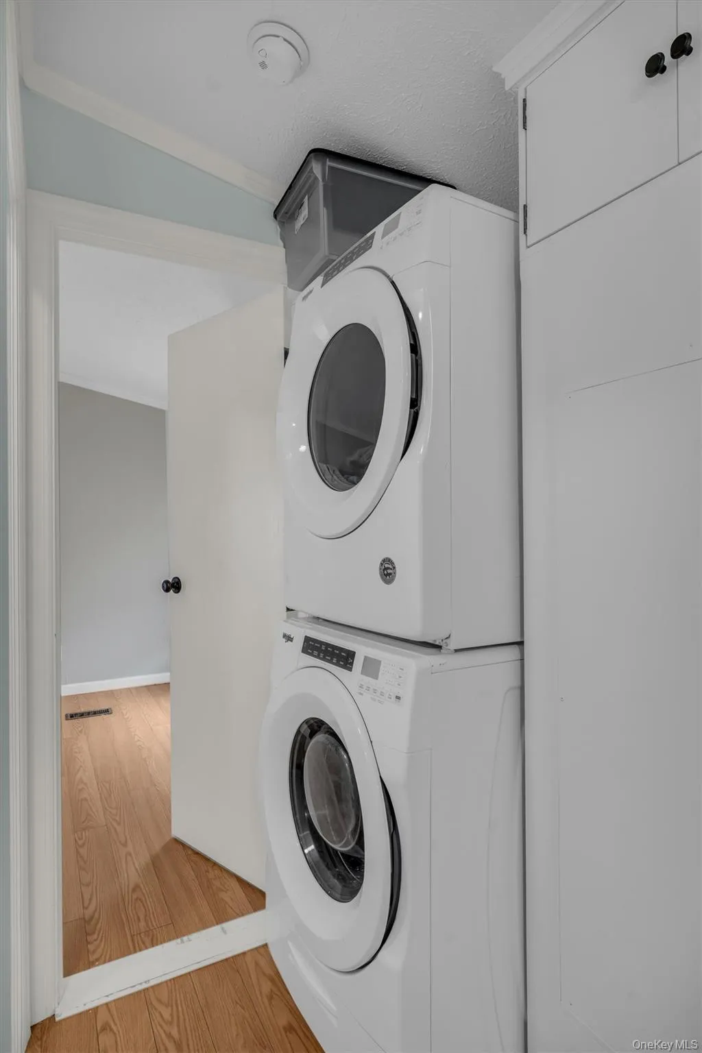 Laundry area with stacked washer / dryer, ornamental molding, and wood finished floors Laundry area with stacked washer / dryer, ornamental molding, and wood finished floors