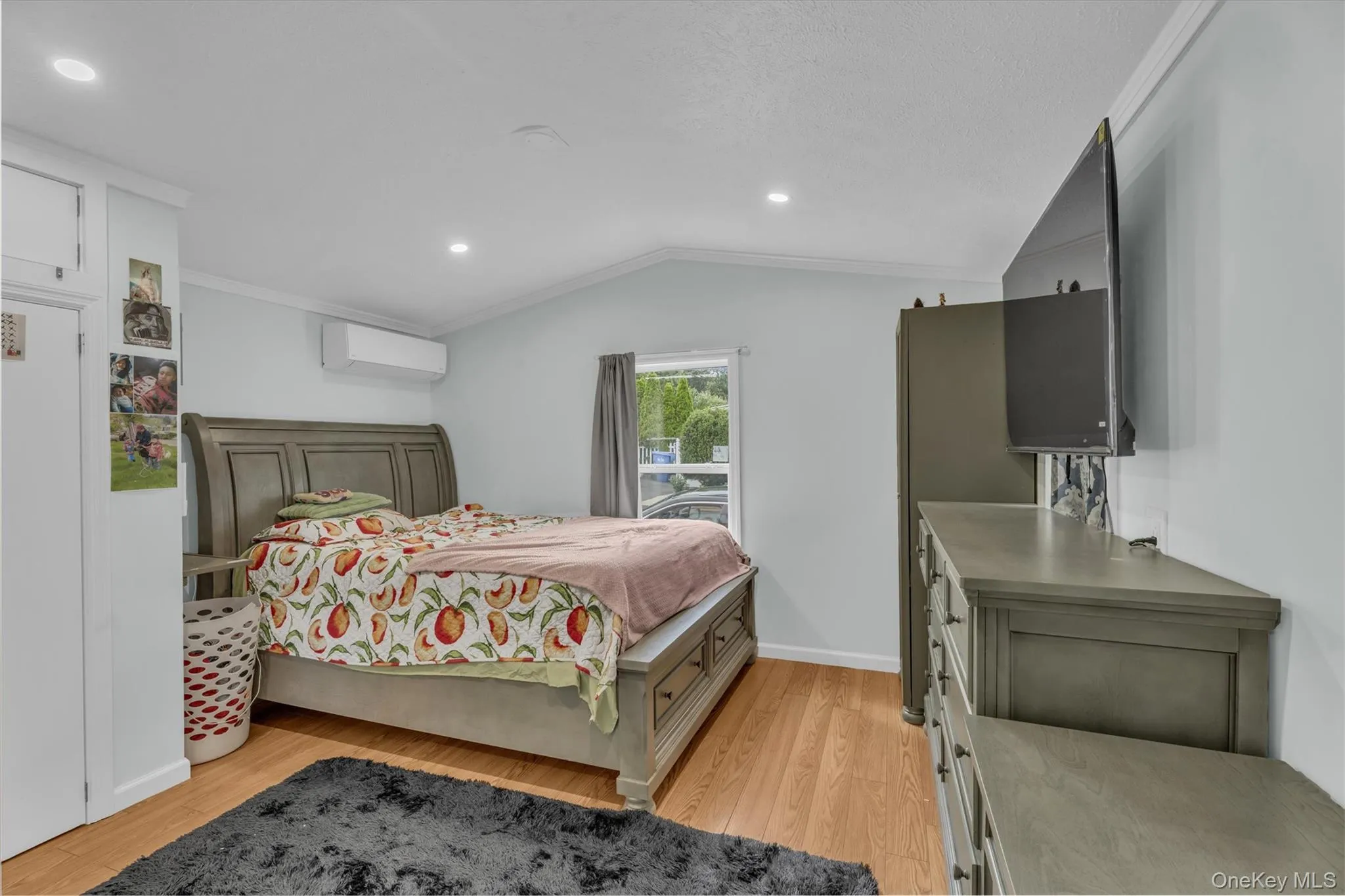 Bedroom featuring ornamental molding, light wood finished floors, lofted ceiling, recessed lighting, and an AC wall unit Bedroom featuring ornamental molding, light wood finished floors, lofted ceiling, recessed lighting, and an AC wall unit