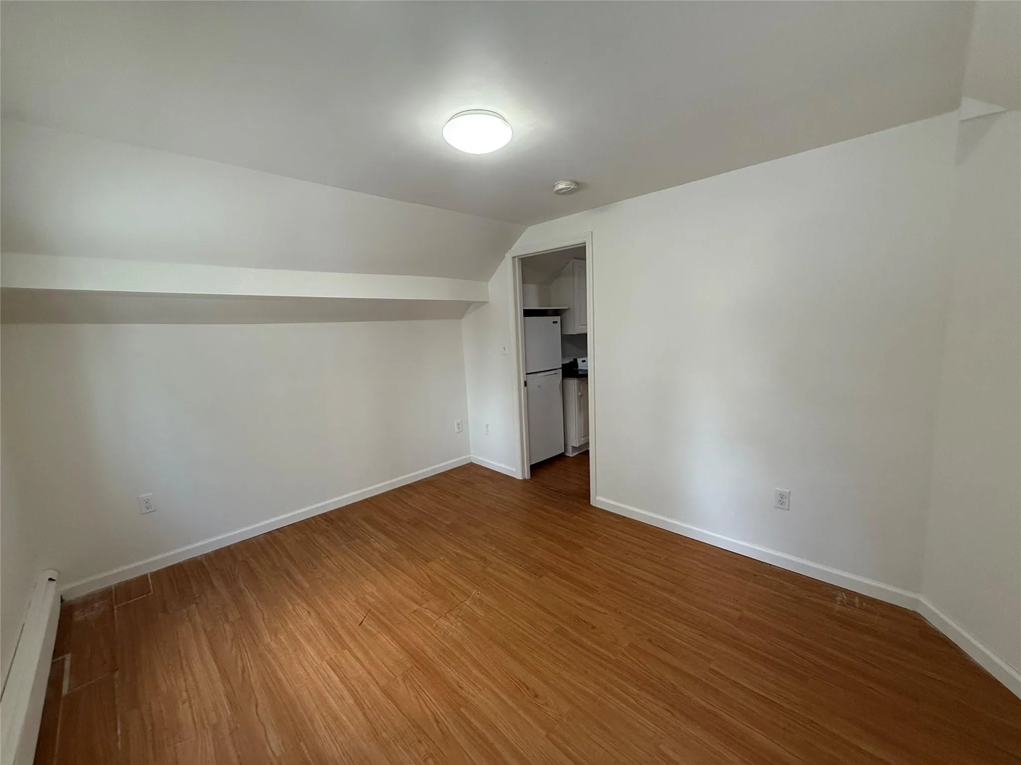 Unfurnished bedroom featuring a baseboard radiator, wood finished floors, vaulted ceiling, freestanding refrigerator, and a spacious closet Unfurnished bedroom featuring a baseboard radiator, wood finished floors, vaulted ceiling, freestanding refrigerator, and a spacious closet