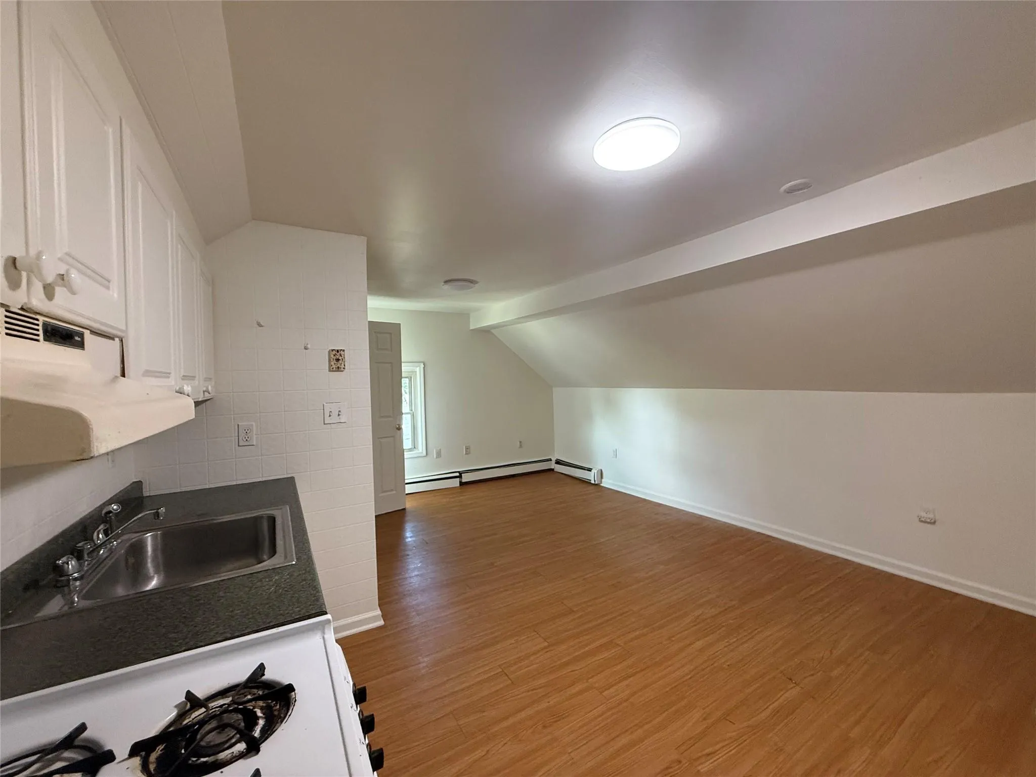 Kitchen with vaulted ceiling, wood finished floors, white cabinets, dark countertops, and stove Kitchen with vaulted ceiling, wood finished floors, white cabinets, dark countertops, and stove