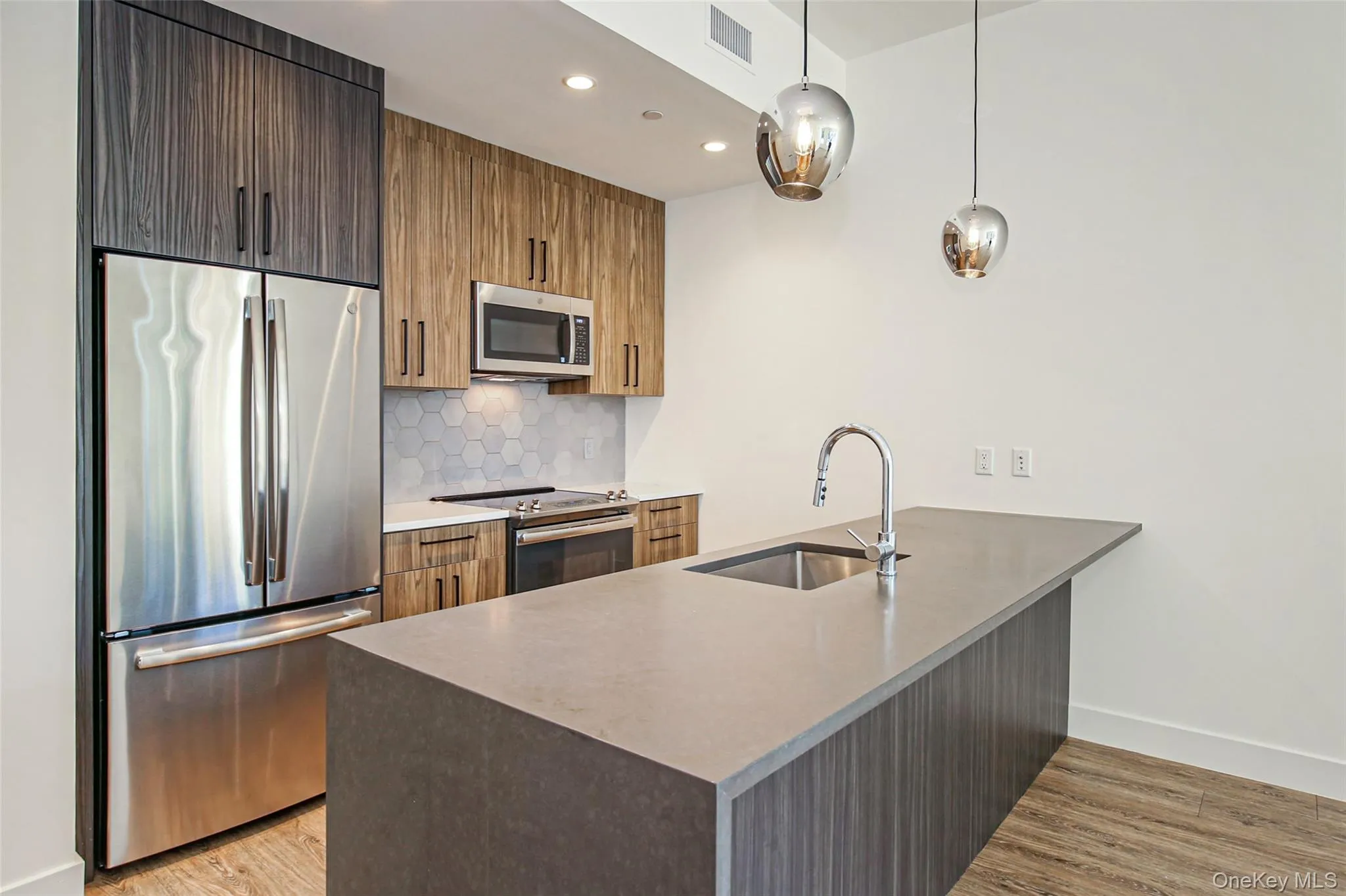 Kitchen with appliances with stainless steel finishes, a peninsula, backsplash, light wood-style floors, and hanging light fixtures Kitchen with appliances with stainless steel finishes, a peninsula, backsplash, light wood-style floors, and hanging light fixtures