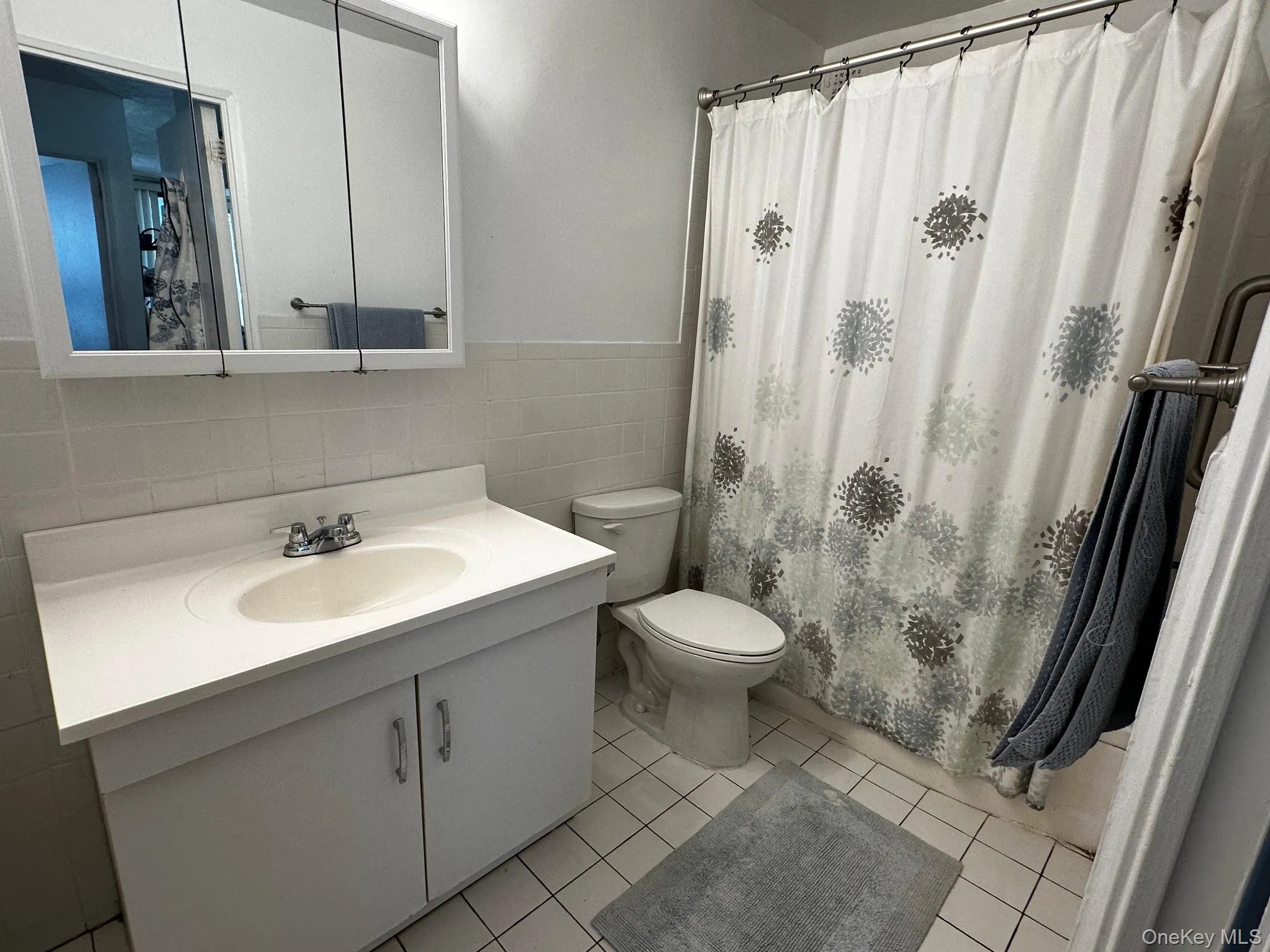 Full bathroom with tile walls, vanity, tile patterned flooring, wainscoting, and a shower with shower curtain Full bathroom with tile walls, vanity, tile patterned flooring, wainscoting, and a shower with shower curtain