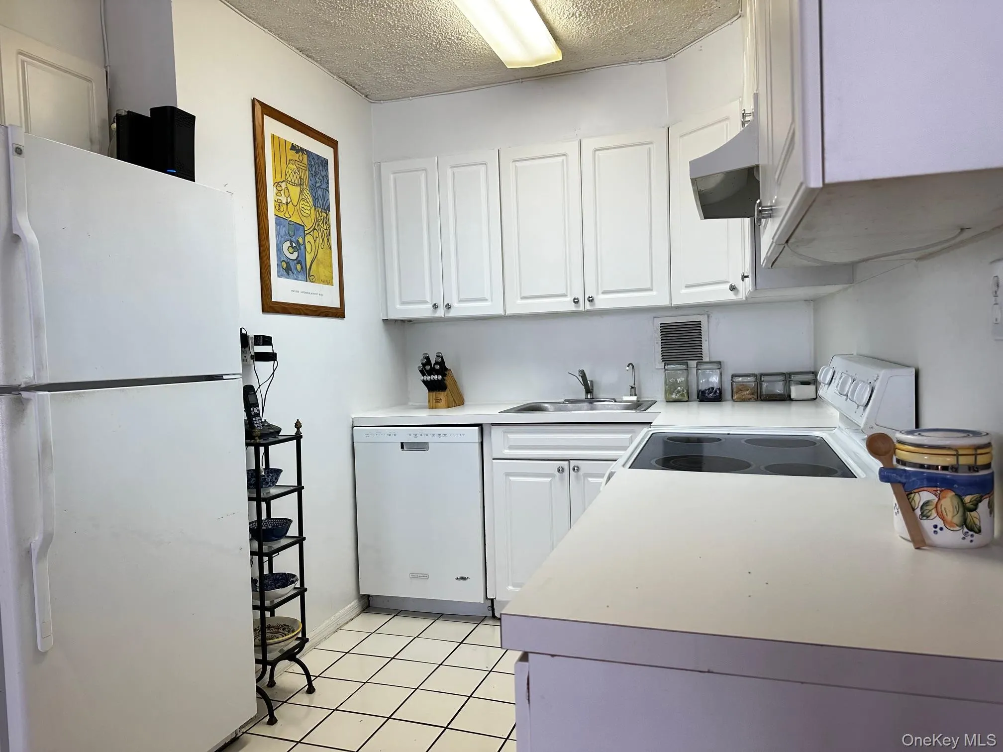 Kitchen with white appliances, light countertops, white cabinetry, and a textured ceiling Kitchen with white appliances, light countertops, white cabinetry, and a textured ceiling