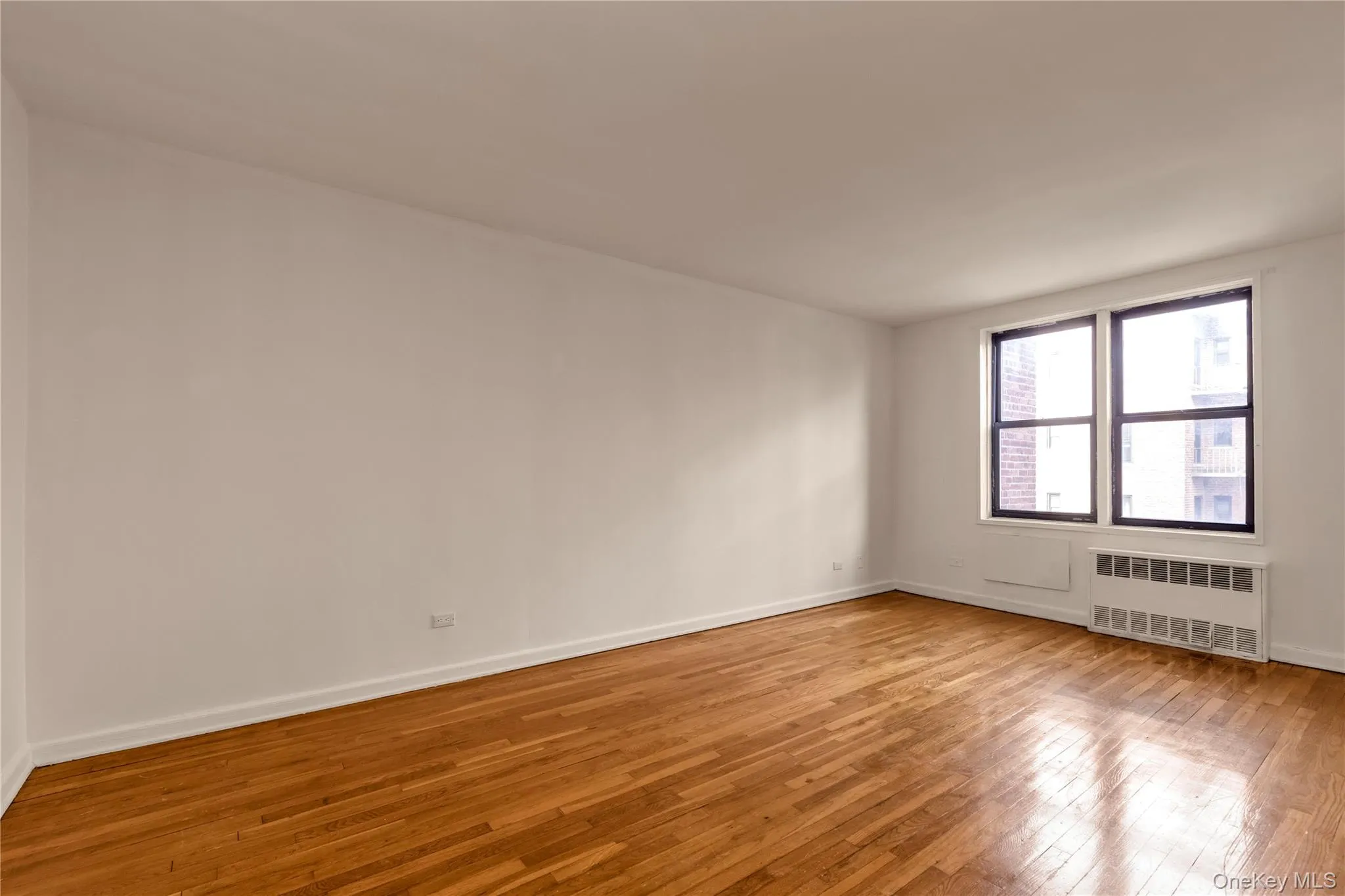 Empty room featuring hardwood / wood-style flooring and radiator heating unit Empty room featuring hardwood / wood-style flooring and radiator heating unit