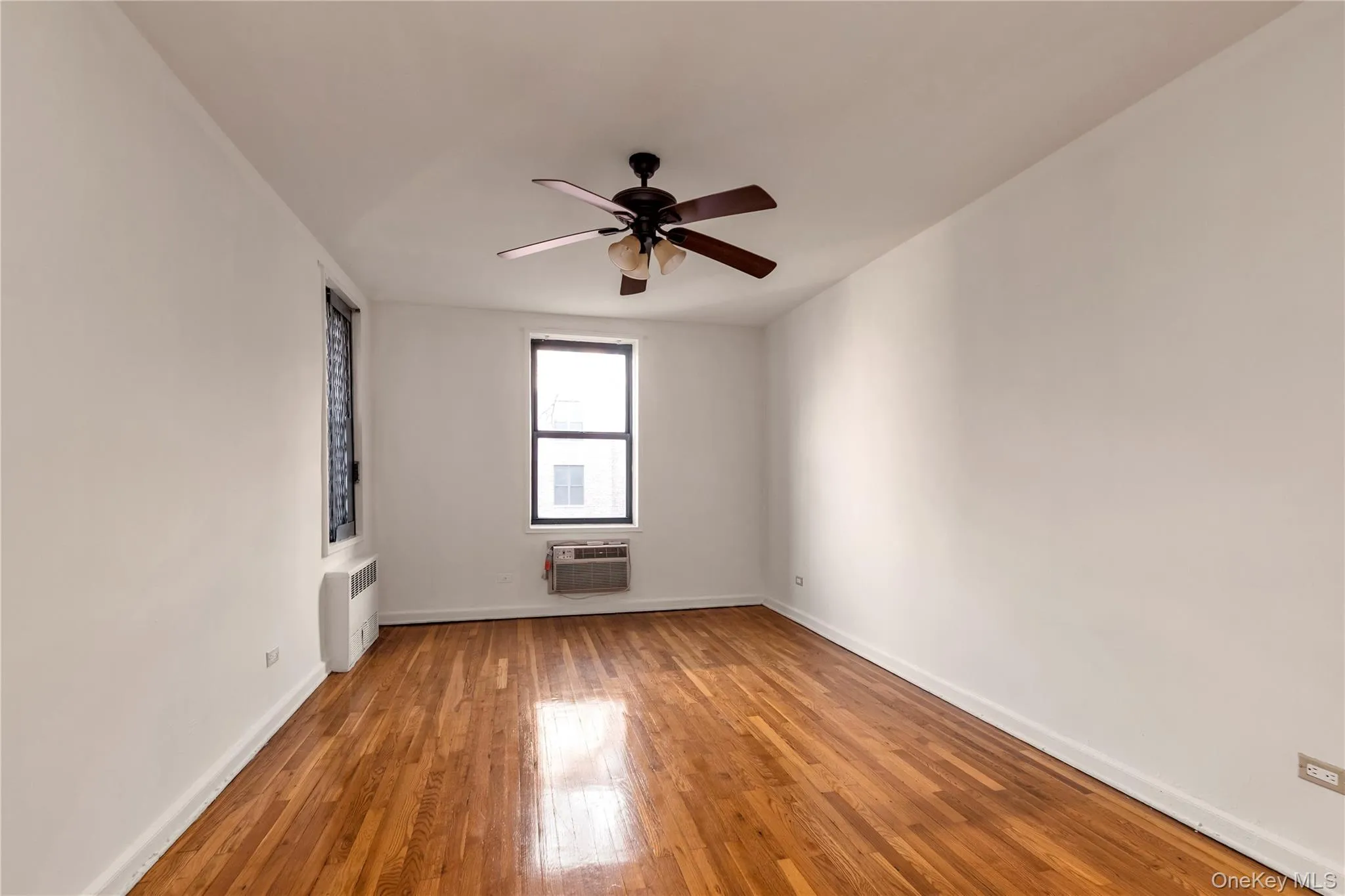Unfurnished room featuring a ceiling fan, radiator, and wood-type flooring Unfurnished room featuring a ceiling fan, radiator, and wood-type flooring