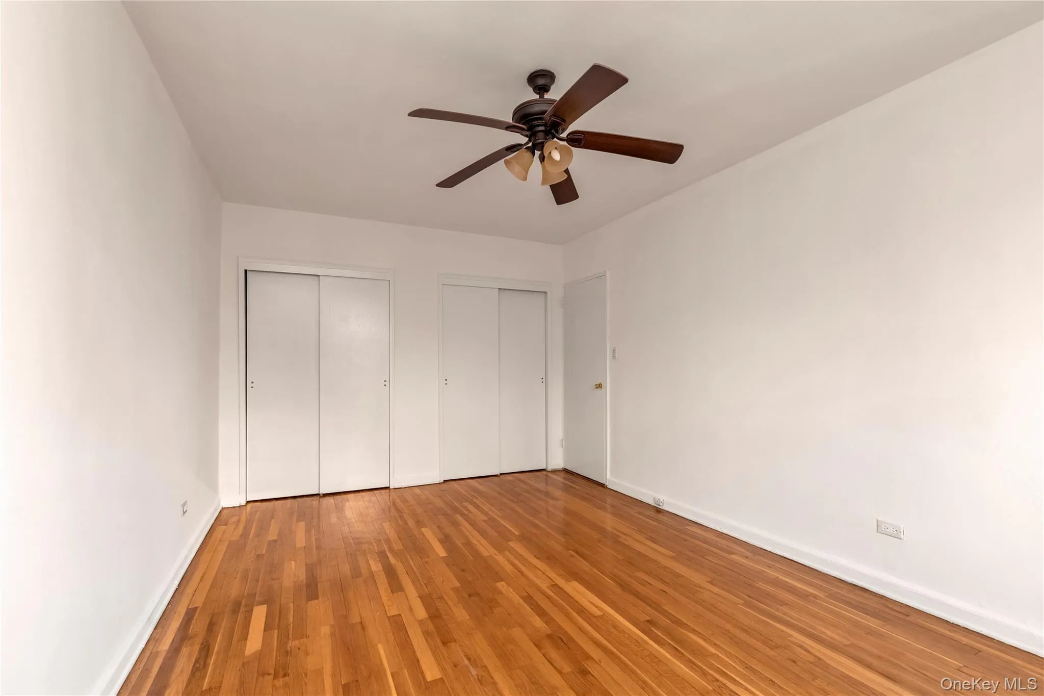 Unfurnished bedroom featuring multiple closets, light wood finished floors, and a ceiling fan Unfurnished bedroom featuring multiple closets, light wood finished floors, and a ceiling fan