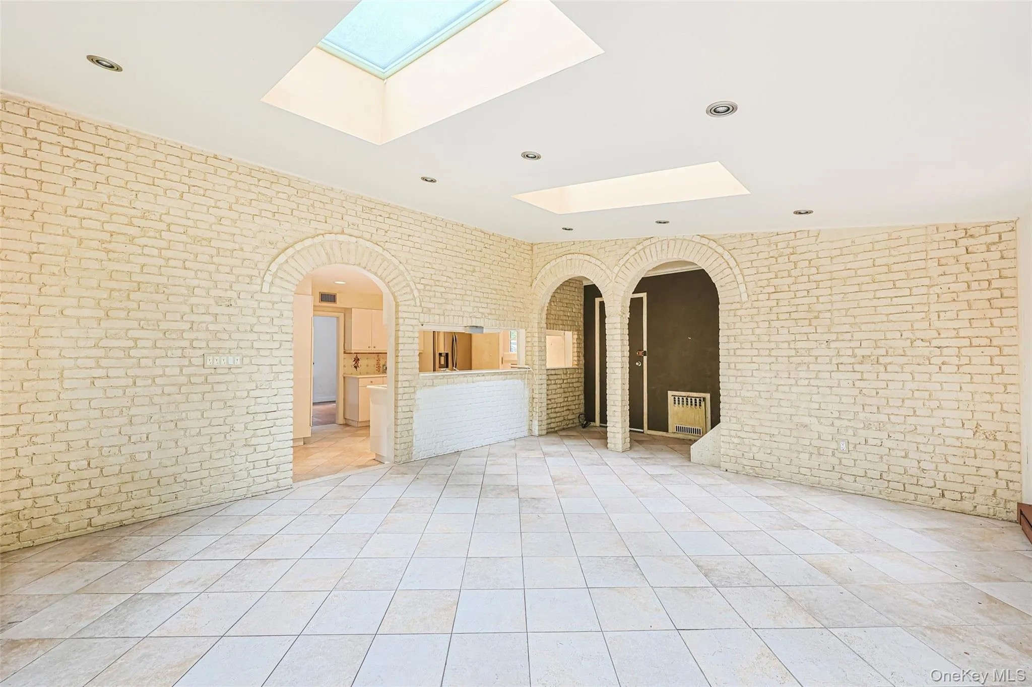 Spare room featuring brick wall, arched walkways, recessed lighting, light tile patterned floors, and a skylight Spare room featuring brick wall, arched walkways, recessed lighting, light tile patterned floors, and a skylight