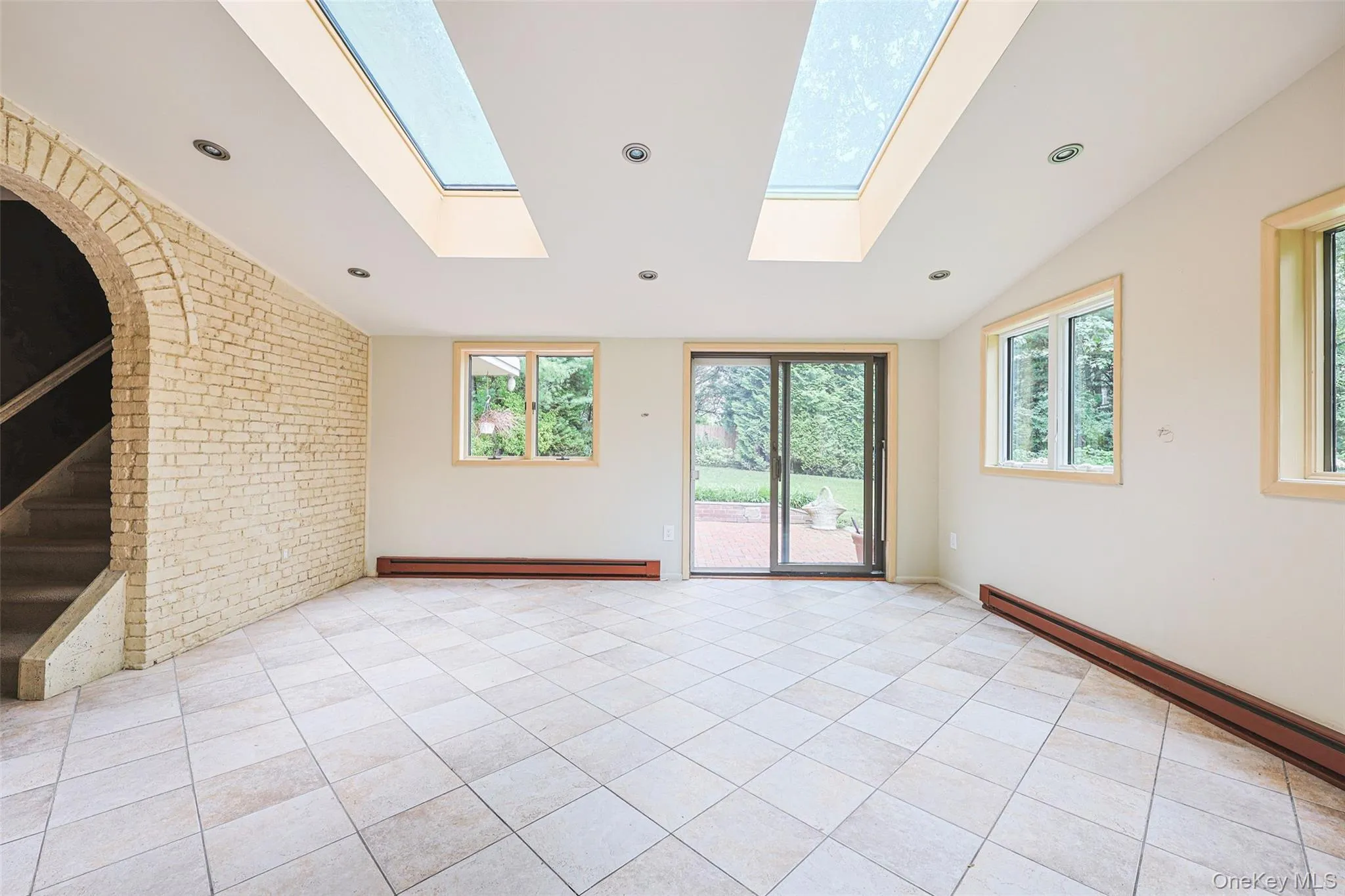 Spare room featuring brick wall, lofted ceiling, light tile patterned floors, a baseboard radiator, and baseboard heating Spare room featuring brick wall, lofted ceiling, light tile patterned floors, a baseboard radiator, and baseboard heating