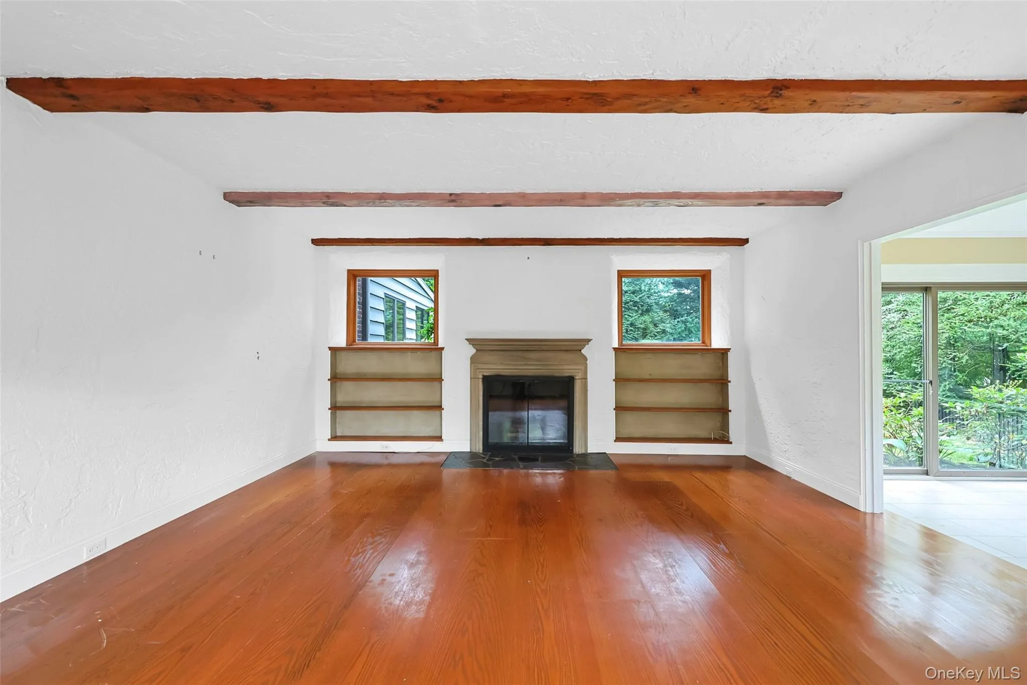 Unfurnished living room with a fireplace with flush hearth, wood finished floors, beamed ceiling, and a textured ceiling Unfurnished living room with a fireplace with flush hearth, wood finished floors, beamed ceiling, and a textured ceiling