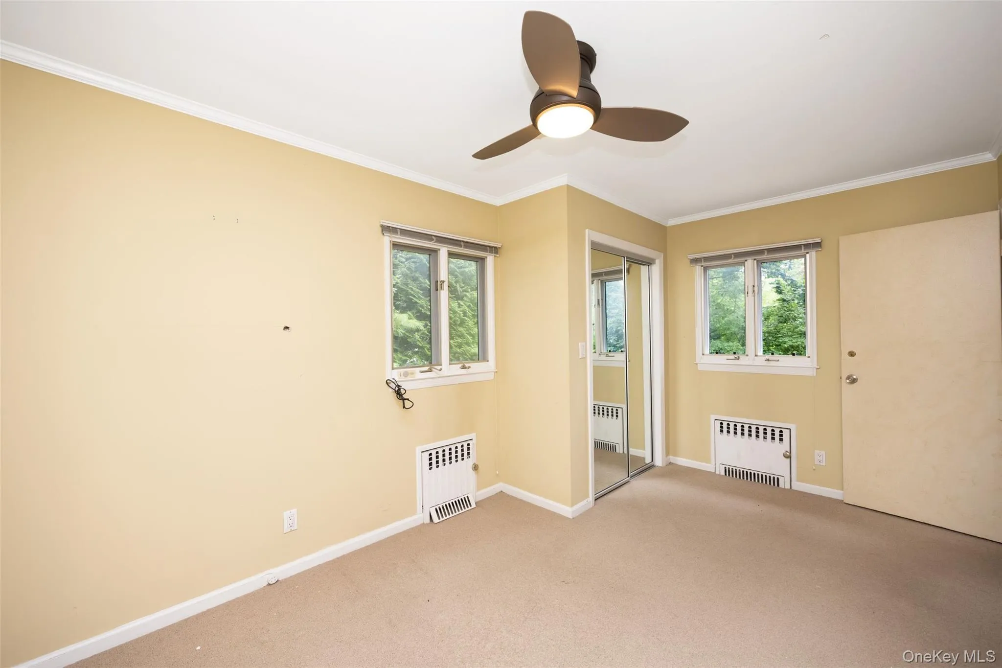 Empty room featuring crown molding, light colored carpet, and radiator heating unit Empty room featuring crown molding, light colored carpet, and radiator heating unit