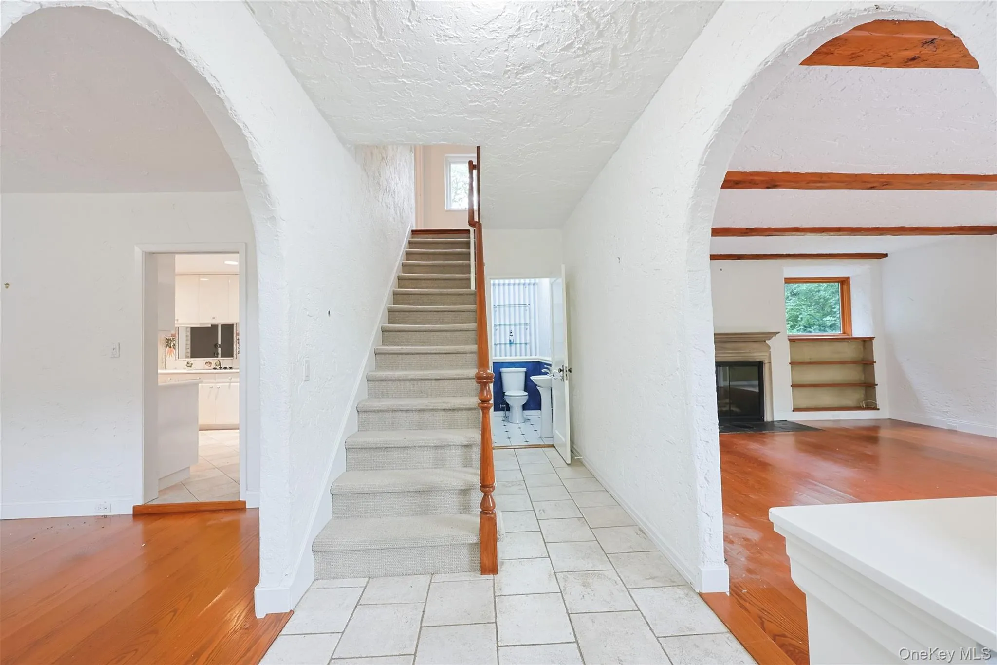 Stairs featuring arched walkways, wood finished floors, a textured ceiling, a fireplace with flush hearth, and beam ceiling Stairs featuring arched walkways, wood finished floors, a textured ceiling, a fireplace with flush hearth, and beam ceiling