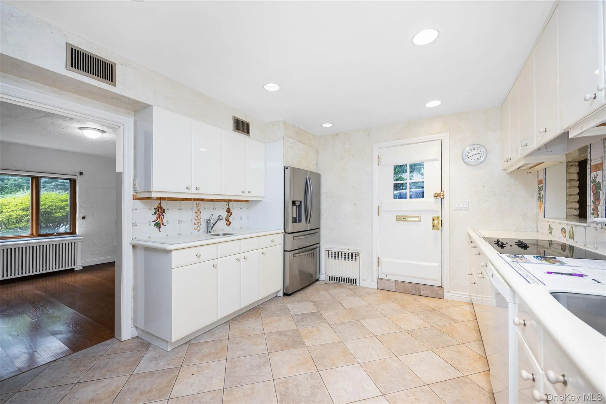 Kitchen featuring plenty of natural light, light countertops, white cabinets, radiator, and recessed lighting Kitchen featuring plenty of natural light, light countertops, white cabinets, radiator, and recessed lighting