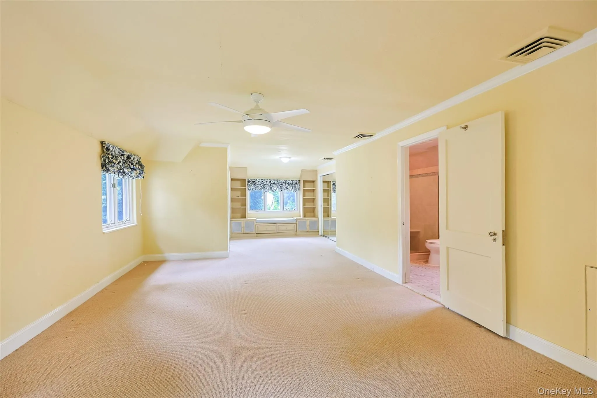 Unfurnished room with a ceiling fan, light carpet, crown molding, and built in features Unfurnished room with a ceiling fan, light carpet, crown molding, and built in features