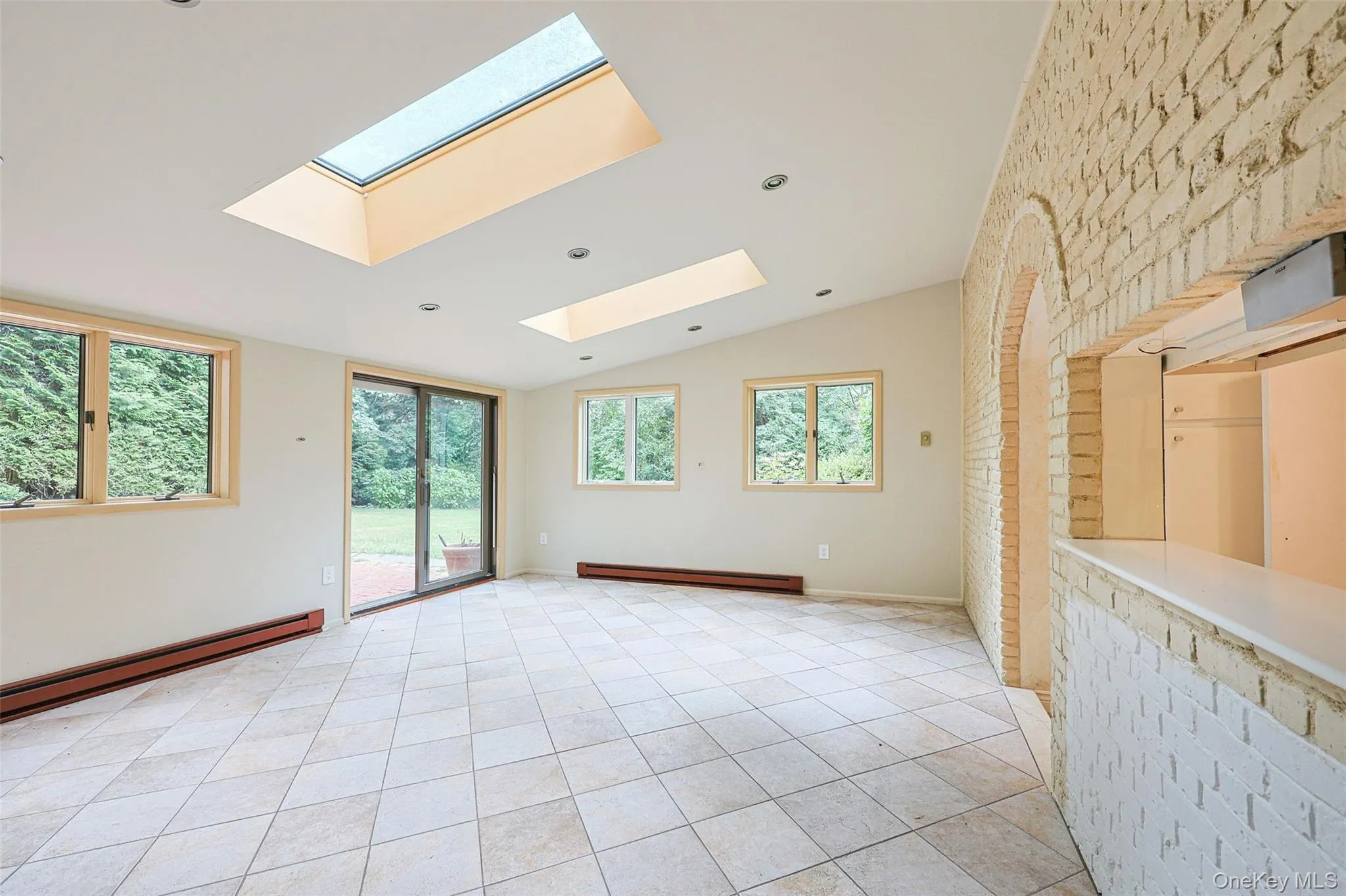 Spare room featuring vaulted ceiling, light tile patterned floors, a baseboard heating unit, and a skylight Spare room featuring vaulted ceiling, light tile patterned floors, a baseboard heating unit, and a skylight