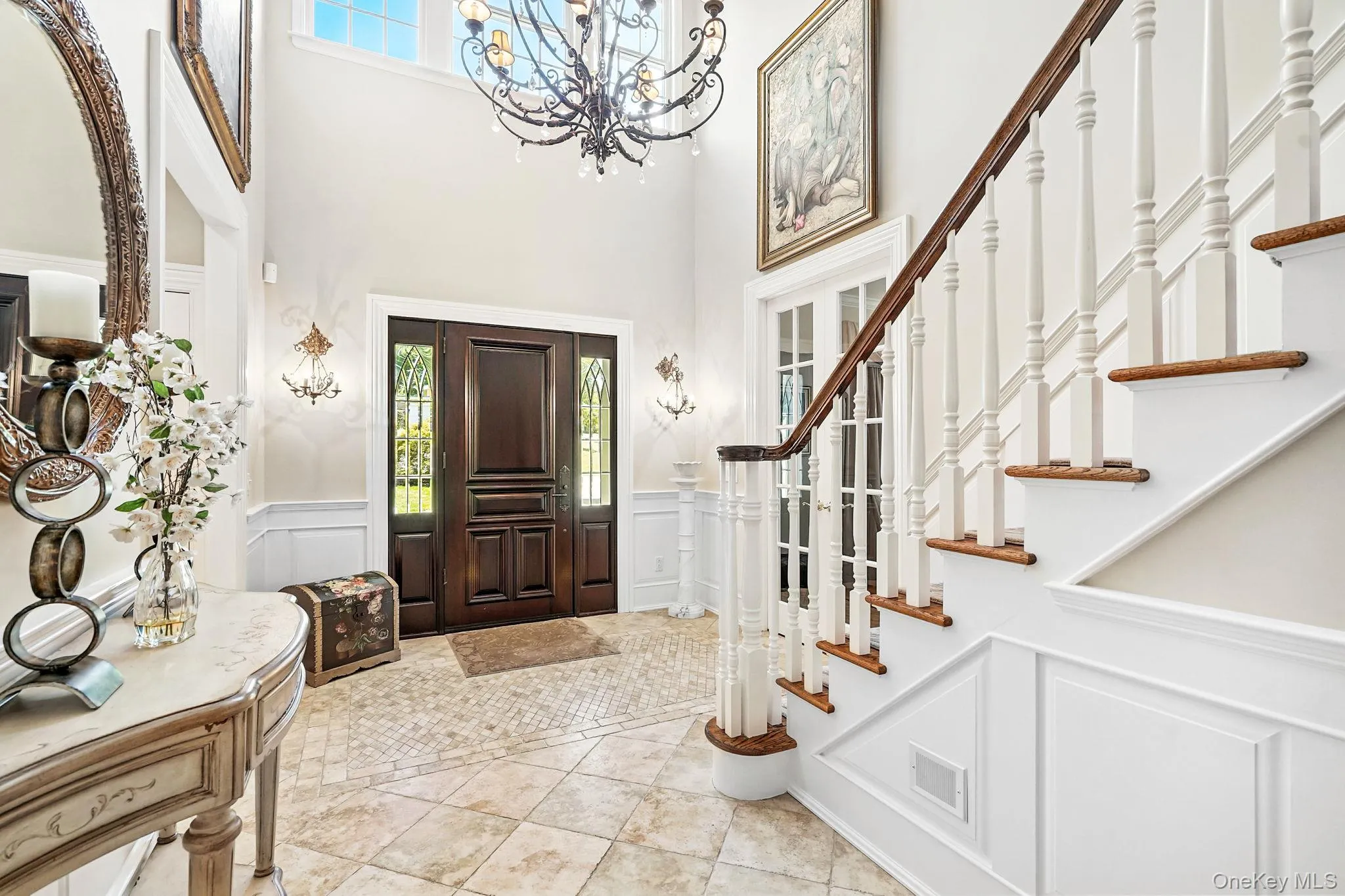 Foyer entrance with a wainscoted wall, a decorative wall, a high ceiling, light tile patterned floors, and stairs Foyer entrance with a wainscoted wall, a decorative wall, a high ceiling, light tile patterned floors, and stairs