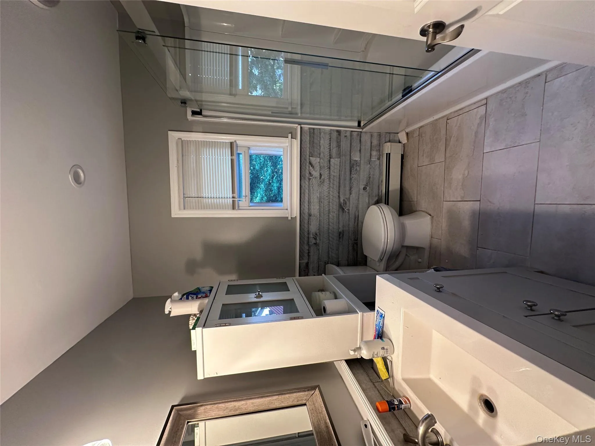 Bathroom with a wainscoted wall, vanity, tile patterned floors, bath / shower combo with glass door, and a baseboard radiator Bathroom with a wainscoted wall, vanity, tile patterned floors, bath / shower combo with glass door, and a baseboard radiator