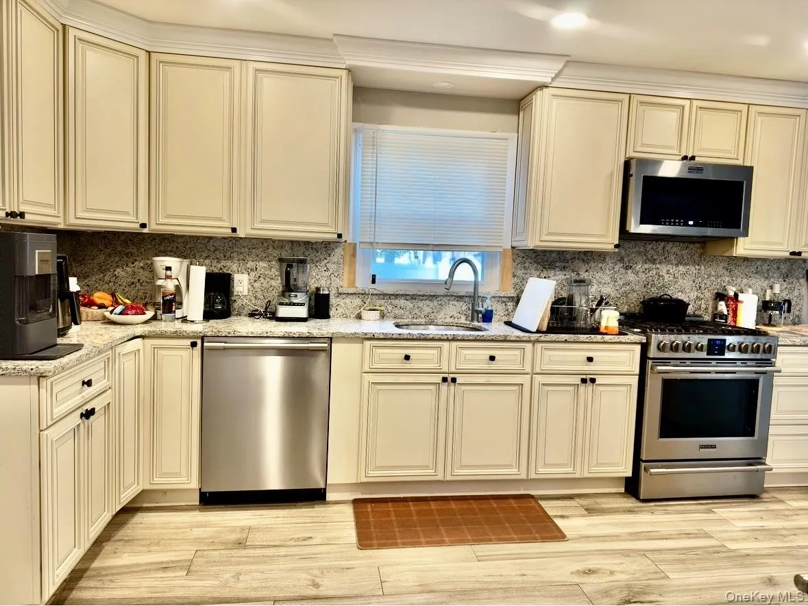 Kitchen with cream cabinets, appliances with stainless steel finishes, light stone countertops, and decorative backsplash Kitchen with cream cabinets, appliances with stainless steel finishes, light stone countertops, and decorative backsplash