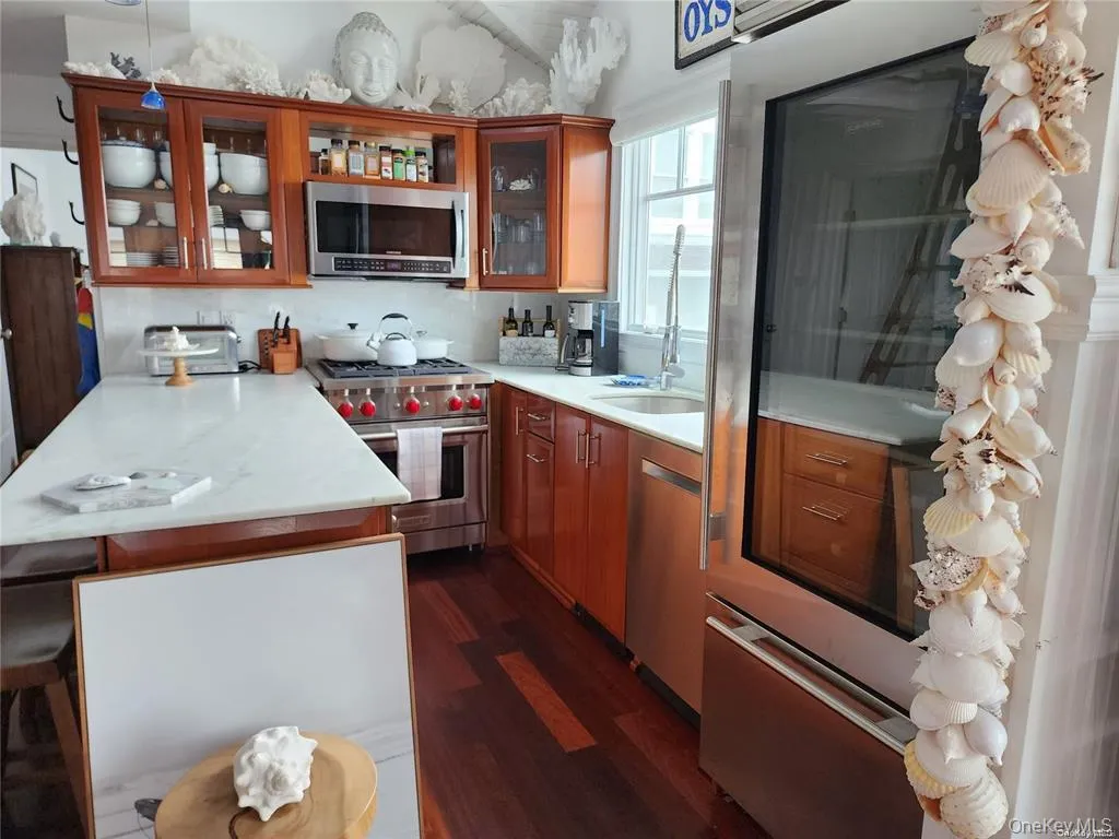 Kitchen with stainless steel appliances, dark wood-type flooring, a peninsula, light countertops, and glass insert cabinets Kitchen with stainless steel appliances, dark wood-type flooring, a peninsula, light countertops, and glass insert cabinets