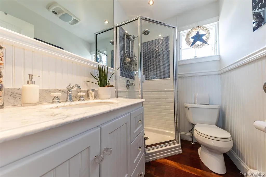 Full bath featuring wainscoting, toilet, vanity, wood finished floors, and a shower stall Full bath featuring wainscoting, toilet, vanity, wood finished floors, and a shower stall