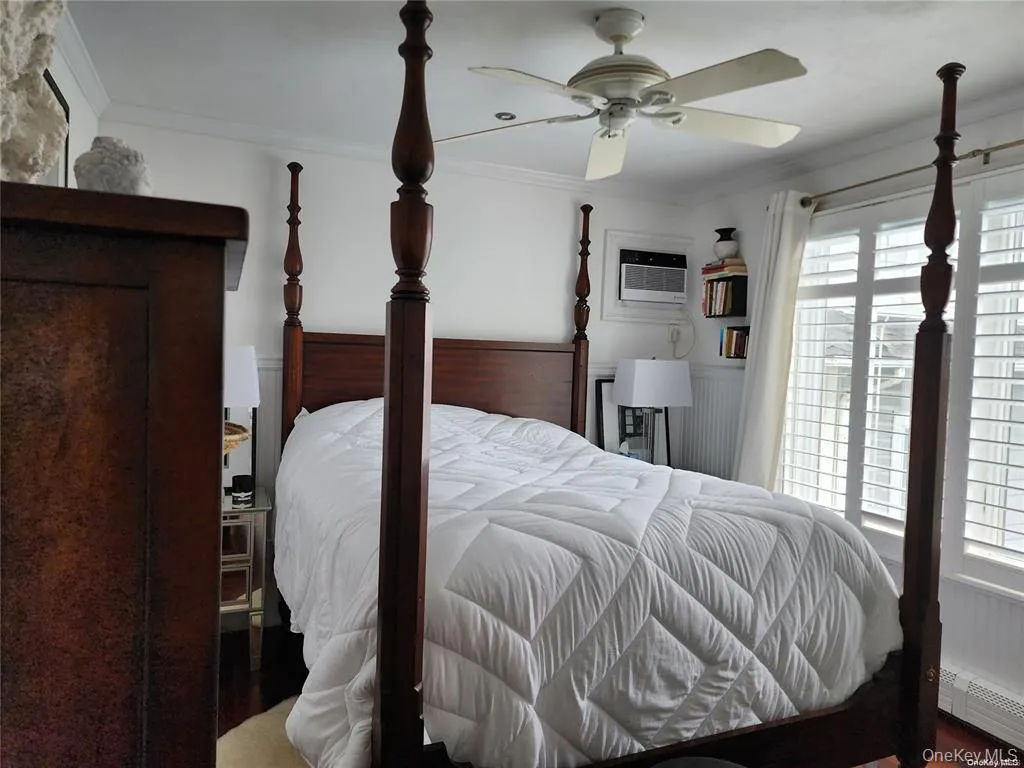 Primary Bedroom featuring ornamental molding, a baseboard heating unit, a ceiling fan, a wainscoted wall, and an AC wall unit Primary Bedroom featuring ornamental molding, a baseboard heating unit, a ceiling fan, a wainscoted wall, and an AC wall unit