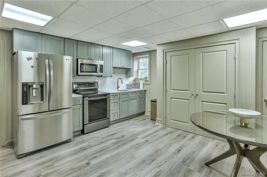 Lower level kitchen featuring appliances with stainless steel finishes, a drop ceiling, light wood finished floors, and light countertops Lower level kitchen featuring appliances with stainless steel finishes, a drop ceiling, light wood finished floors, and light countertops