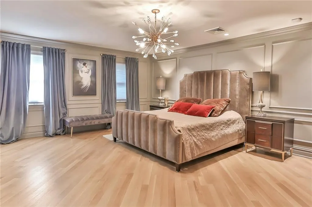 Bedroom featuring a decorative wall, a chandelier, light wood-style flooring, and ornamental molding Bedroom featuring a decorative wall, a chandelier, light wood-style flooring, and ornamental molding