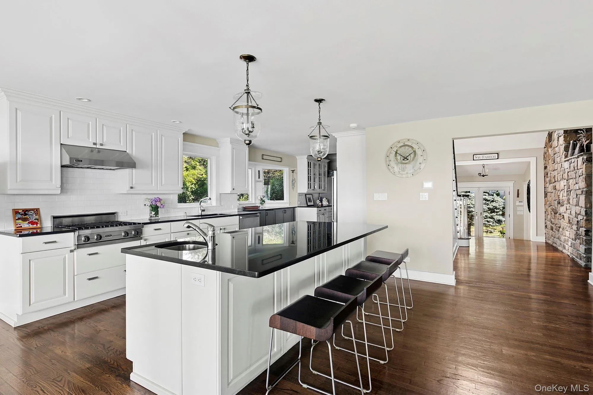 Kitchen with dark wood-style flooring, dark countertops, decorative backsplash, a center island with sink, and under cabinet range hood Kitchen with dark wood-style flooring, dark countertops, decorative backsplash, a center island with sink, and under cabinet range hood