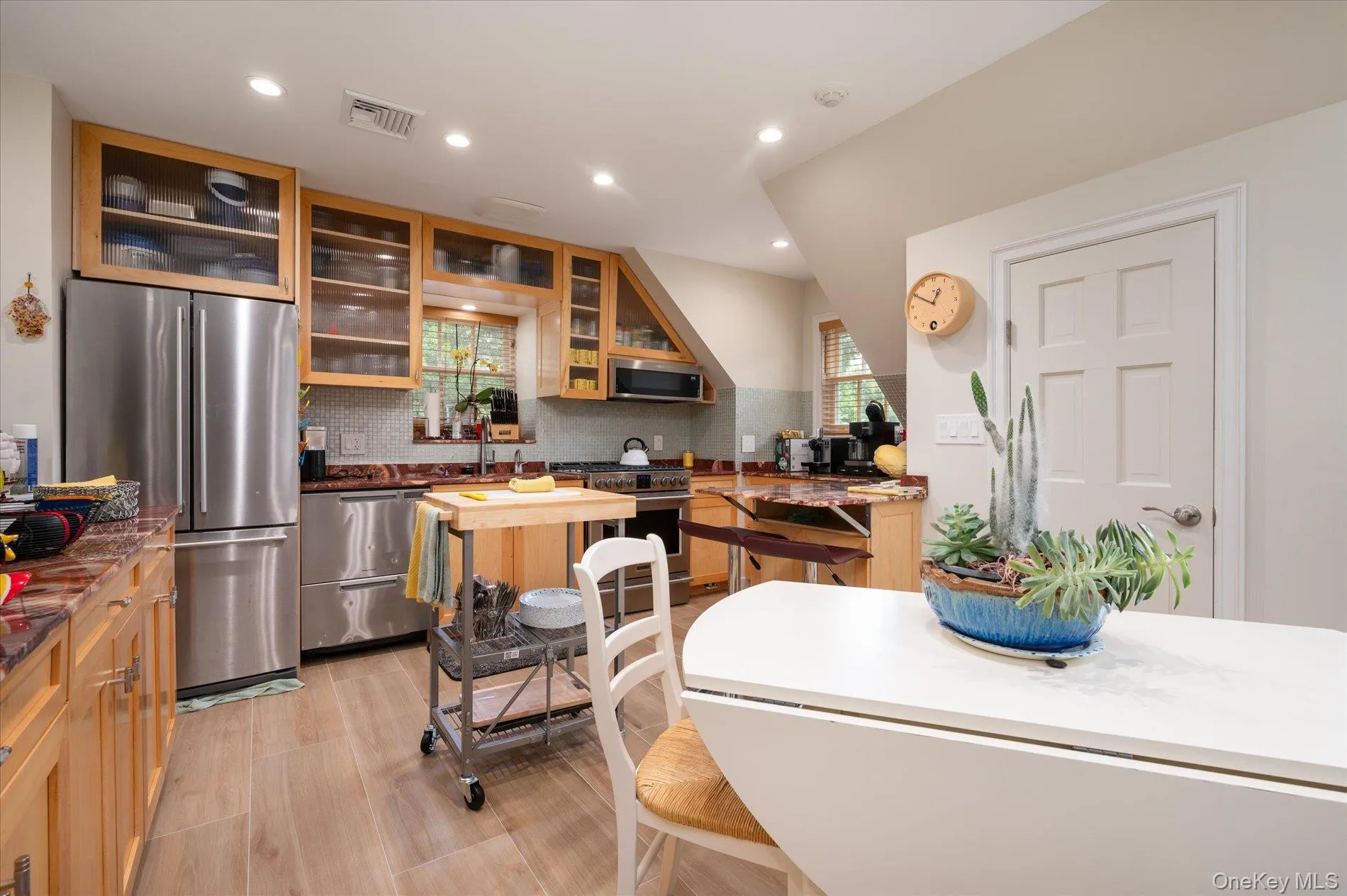 Kitchen with appliances with stainless steel finishes, light wood-style floors, glass insert cabinets, recessed lighting, and backsplash Kitchen with appliances with stainless steel finishes, light wood-style floors, glass insert cabinets, recessed lighting, and backsplash