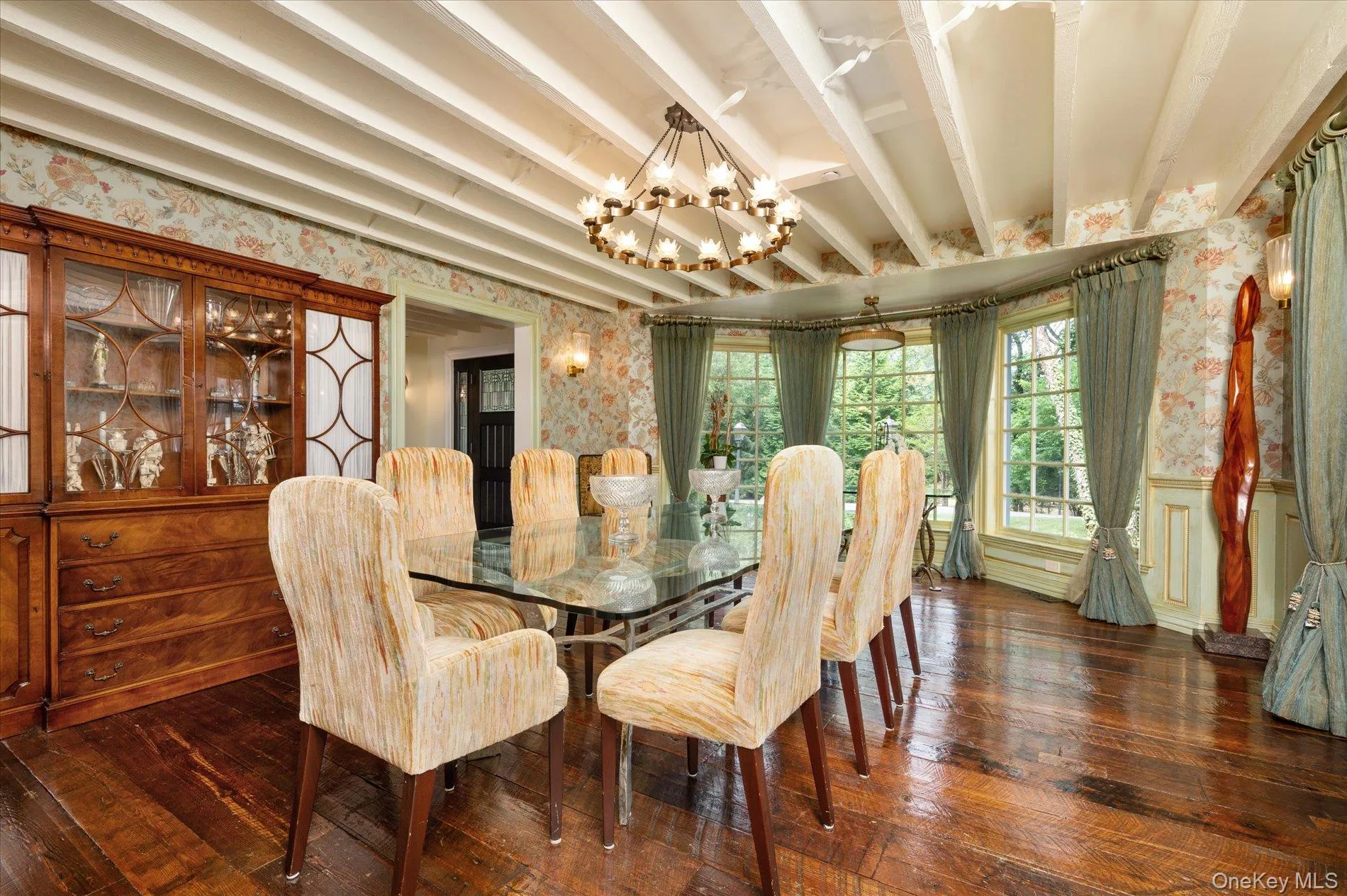 Dining area featuring wallpapered walls, a chandelier, hardwood / wood-style flooring, beam ceiling, and wainscoting Dining area featuring wallpapered walls, a chandelier, hardwood / wood-style flooring, beam ceiling, and wainscoting