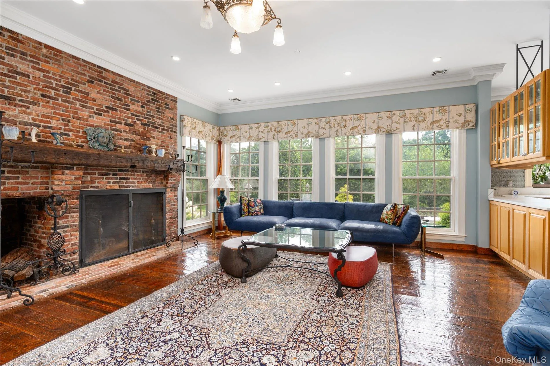 Living room featuring hardwood / wood-style flooring, crown molding, a brick fireplace, recessed lighting, and a chandelier Living room featuring hardwood / wood-style flooring, crown molding, a brick fireplace, recessed lighting, and a chandelier