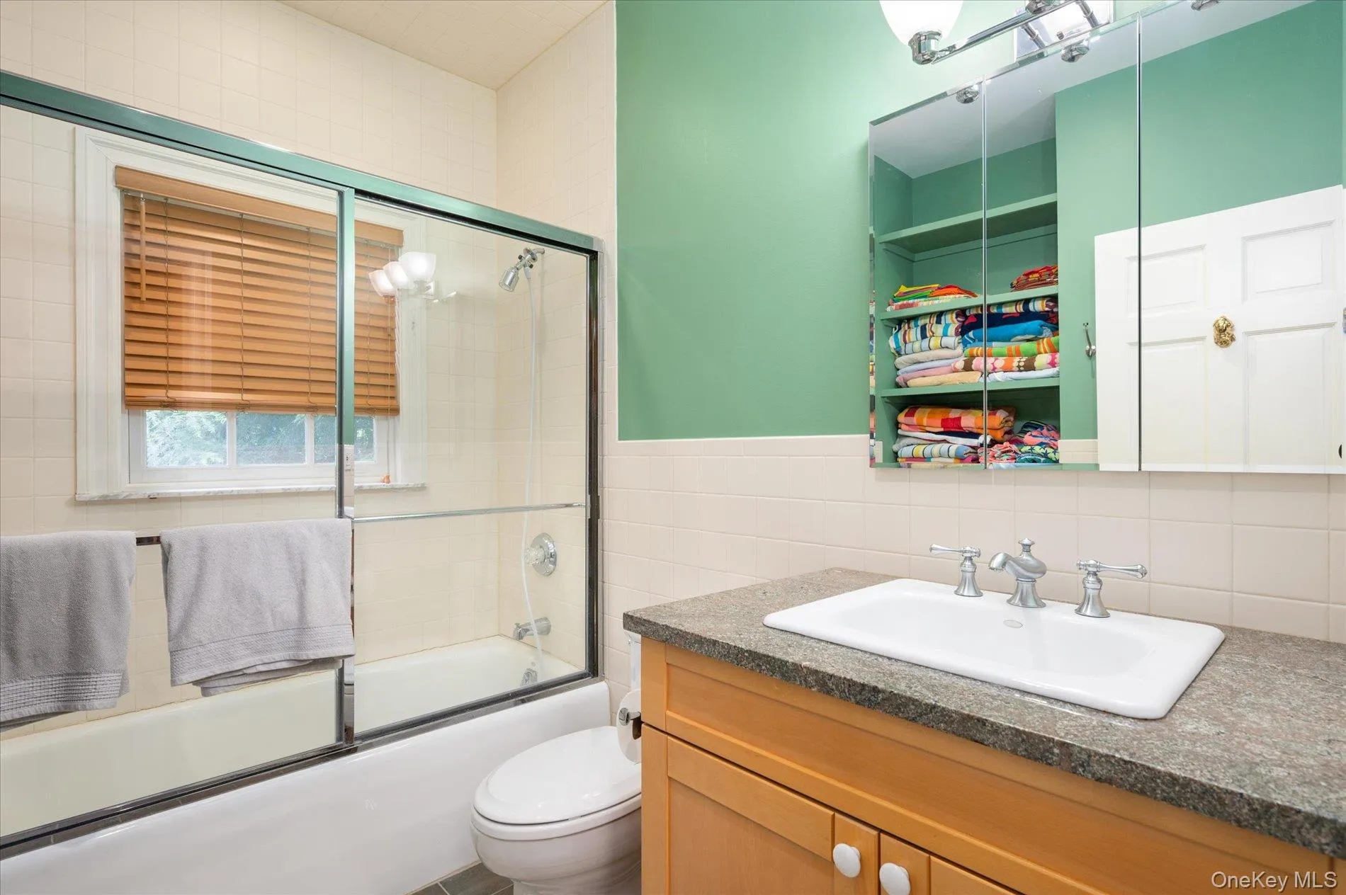 Bathroom featuring tile walls, vanity, combined bath / shower with glass door, and wainscoting Bathroom featuring tile walls, vanity, combined bath / shower with glass door, and wainscoting