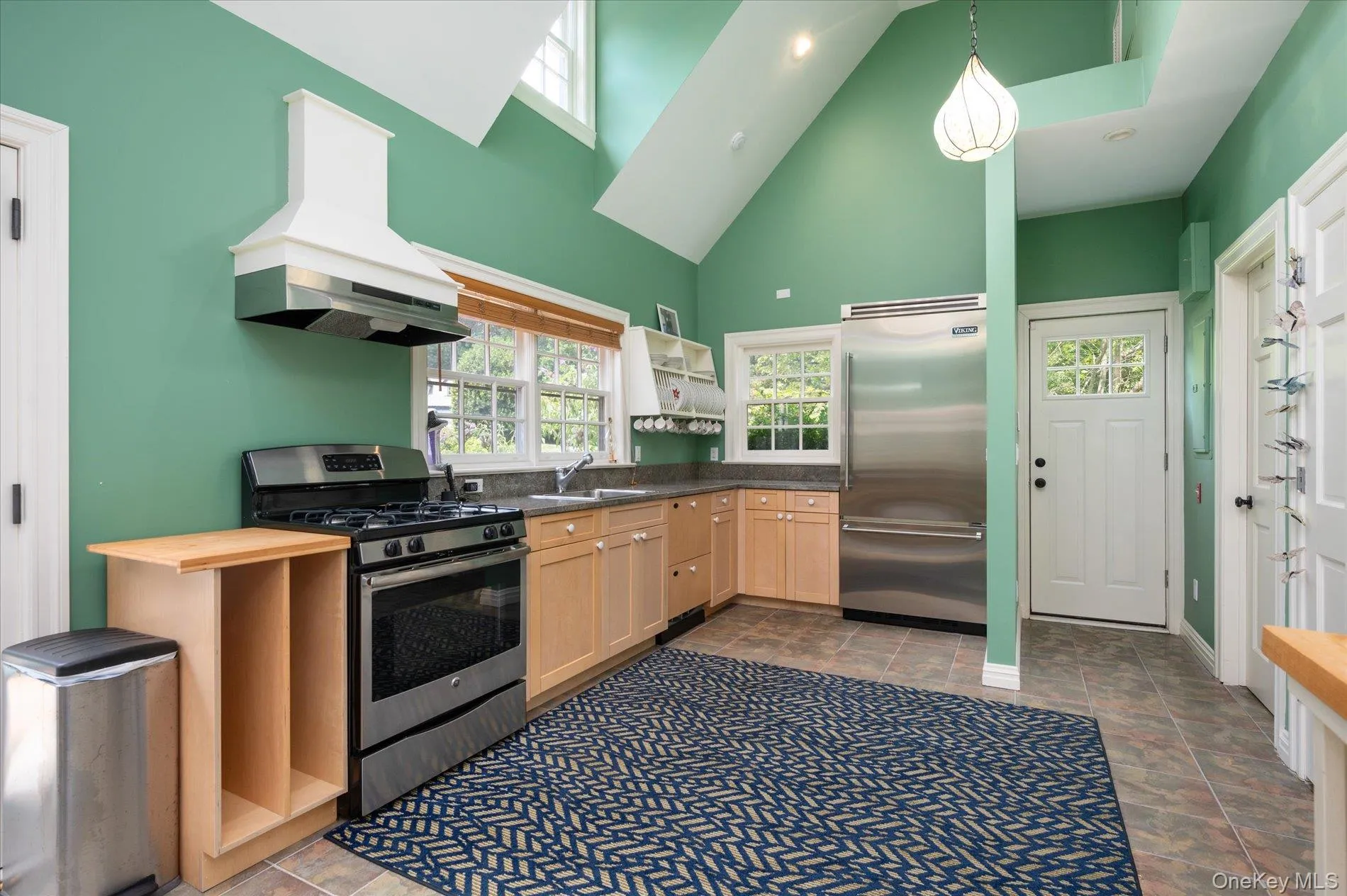 Kitchen with stainless steel appliances, custom range hood, light brown cabinetry, stone finish floors, and butcher block countertops Kitchen with stainless steel appliances, custom range hood, light brown cabinetry, stone finish floors, and butcher block countertops