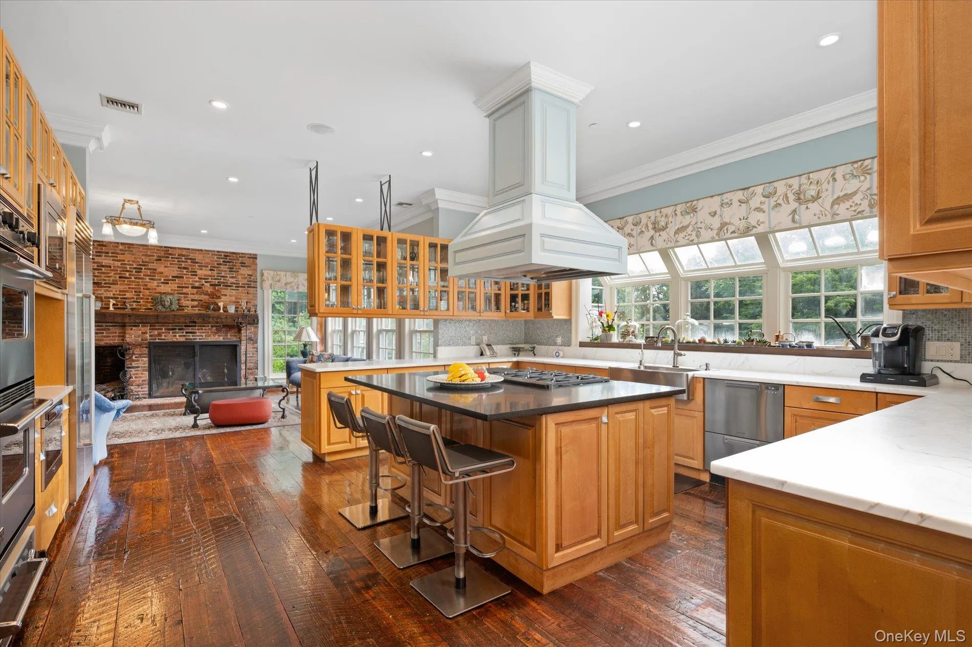 Kitchen featuring ornamental molding, dark wood finished floors, a fireplace, a center island, and glass insert cabinets Kitchen featuring ornamental molding, dark wood finished floors, a fireplace, a center island, and glass insert cabinets