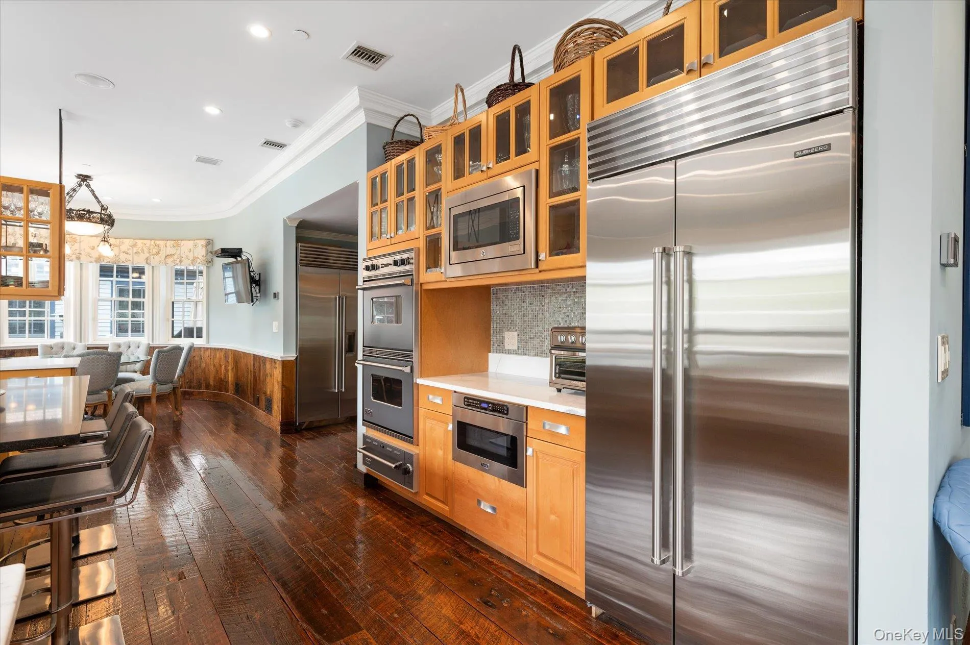 Kitchen featuring wainscoting, built in appliances, crown molding, dark wood-style floors, and light countertops Kitchen featuring wainscoting, built in appliances, crown molding, dark wood-style floors, and light countertops