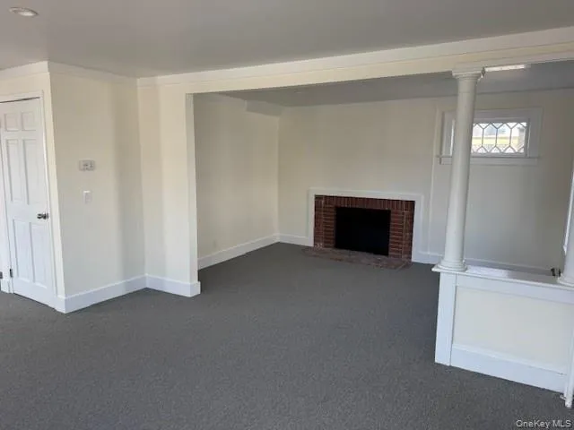Unfurnished living room featuring ornamental molding, dark colored carpet, and a fireplace Unfurnished living room featuring ornamental molding, dark colored carpet, and a fireplace