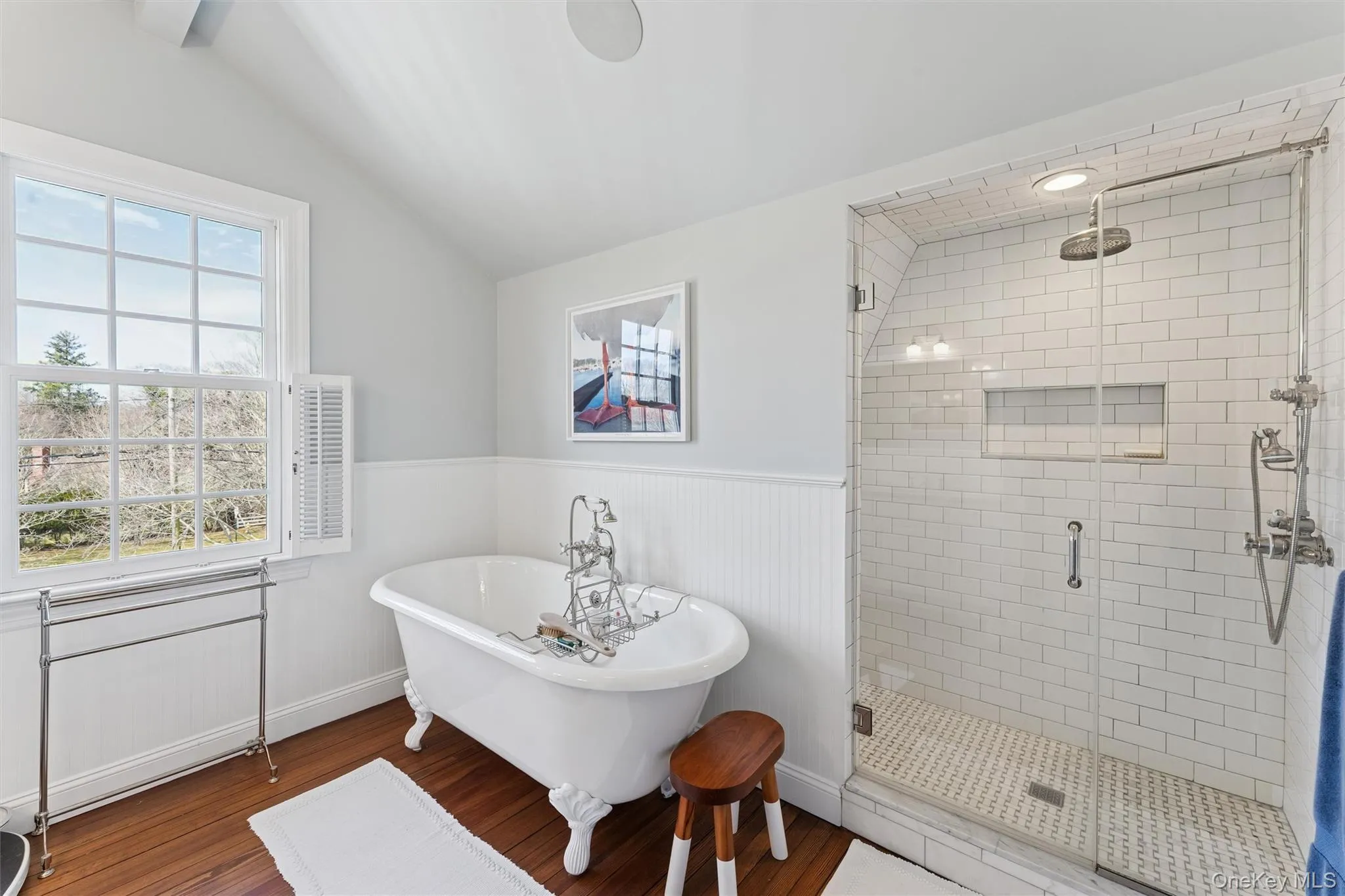 Bathroom featuring wood finished floors, a shower stall, wainscoting, lofted ceiling, and a freestanding bath Bathroom featuring wood finished floors, a shower stall, wainscoting, lofted ceiling, and a freestanding bath