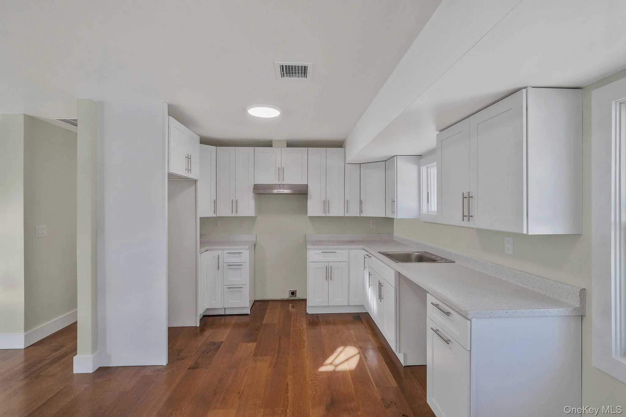 Kitchen with dark wood-style flooring, white cabinets, light countertops, and under cabinet range hood Kitchen with dark wood-style flooring, white cabinets, light countertops, and under cabinet range hood