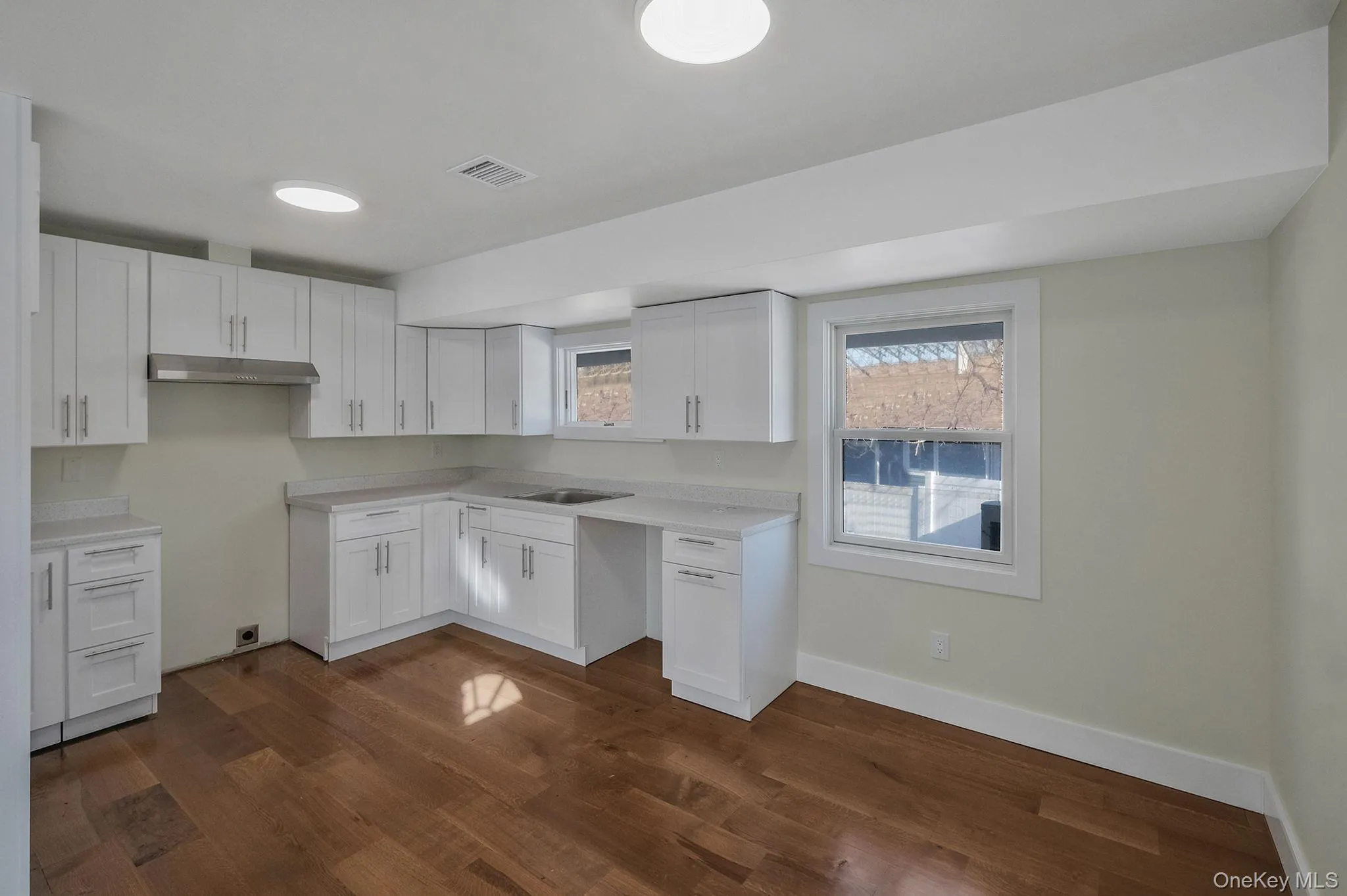 Kitchen with dark wood-style floors, healthy amount of natural light, white cabinetry, and light countertops Kitchen with dark wood-style floors, healthy amount of natural light, white cabinetry, and light countertops